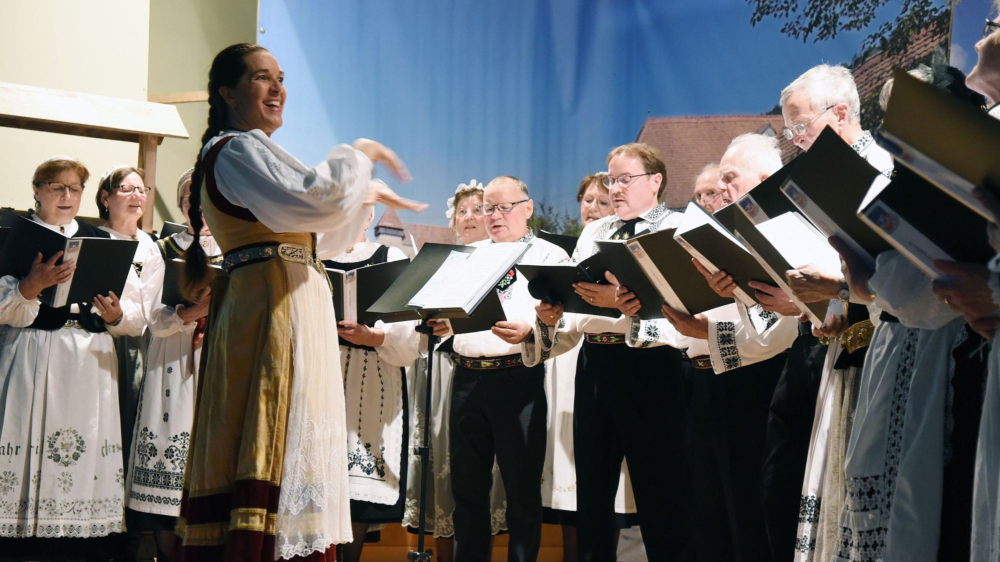 Sängerinnen und Sänger in Tracht gruppieren sich um ihre Dirigentin.