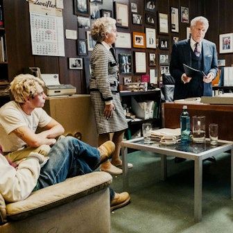 Symcha Zweifler steht hinter seinem Schreibtisch. Er schaut ernst, hält eine Mappe in seiner Hand. Seine Frau Lilka steht an der Ecke des Tisches, seine Tochter Mimi sitzt auf dem Stuhl ihm gegenüber. Die Enkel Samuel und Leon sitzen auf einer Couch an der Seite. Alle stehen Symcha ernst an. Im Hintergrund hängen Urkunden, Fotos, Kalender und andere Erinnerungen an der Wand.