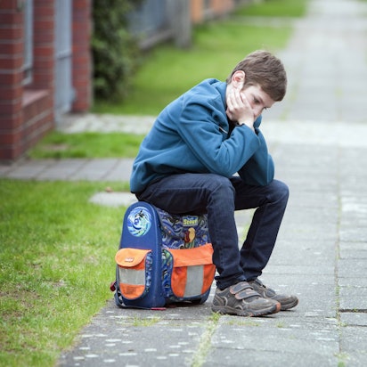 Trauriges Kind sitzt auf seinem Schulranzen