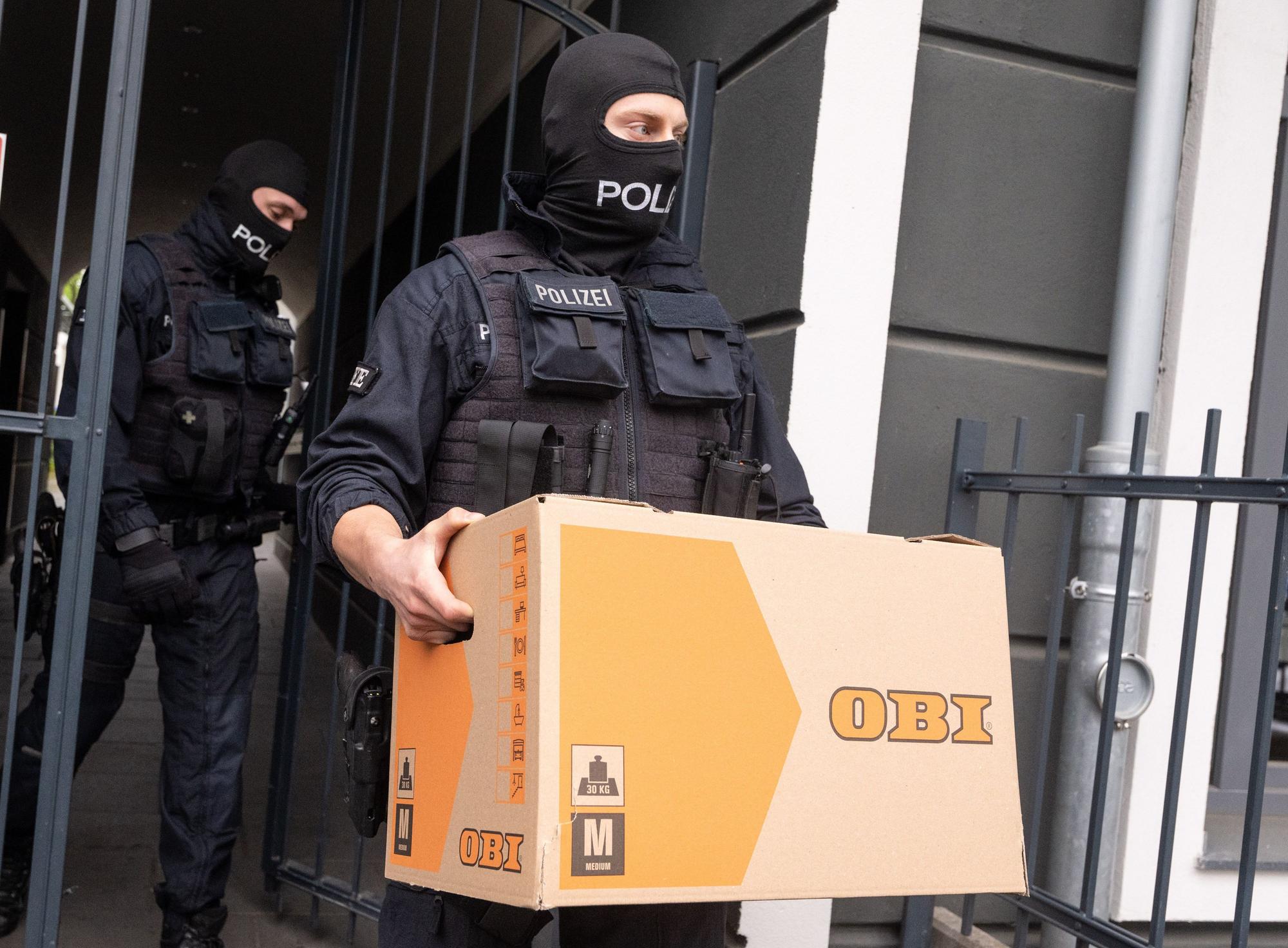 Ein Polizist trägt im Rahmen der Razzia gegen Schleuser in Bonn einen Karton mit Beweismaterial aus einem Gebäude.
