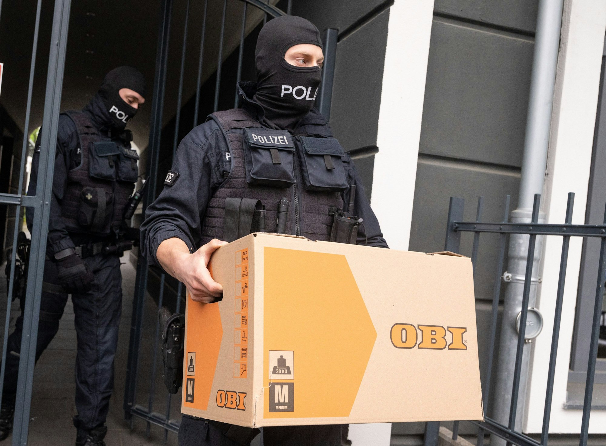 Ein Polizist trägt im Rahmen der Razzia gegen Schleuser in Bonn einen Karton mit Beweismaterial aus einem Gebäude.