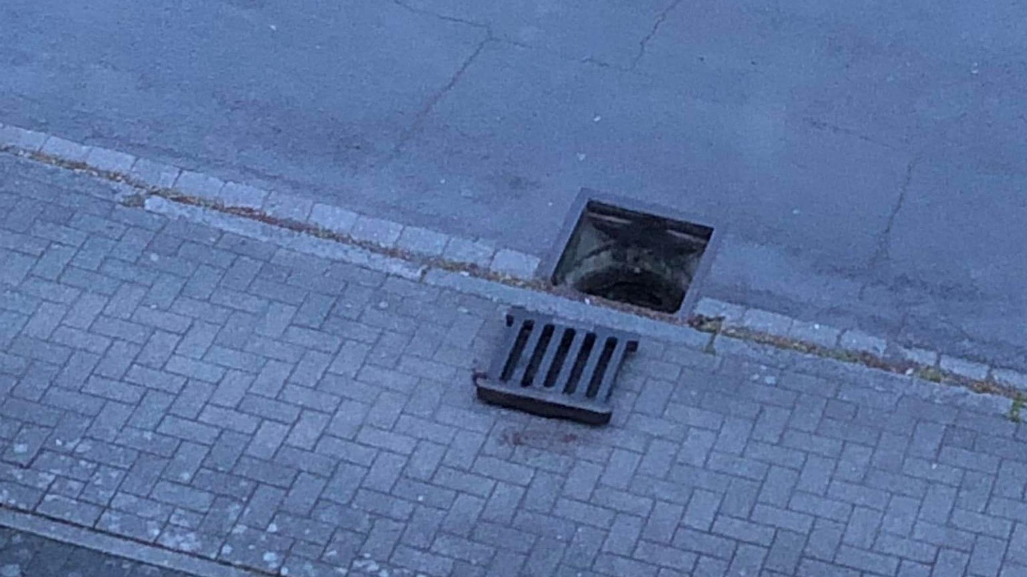 Auf dem Foto ist zu sehen, wie ein Gullydeckel nehmen dem Schacht auf dem Bürgersteig liegt.