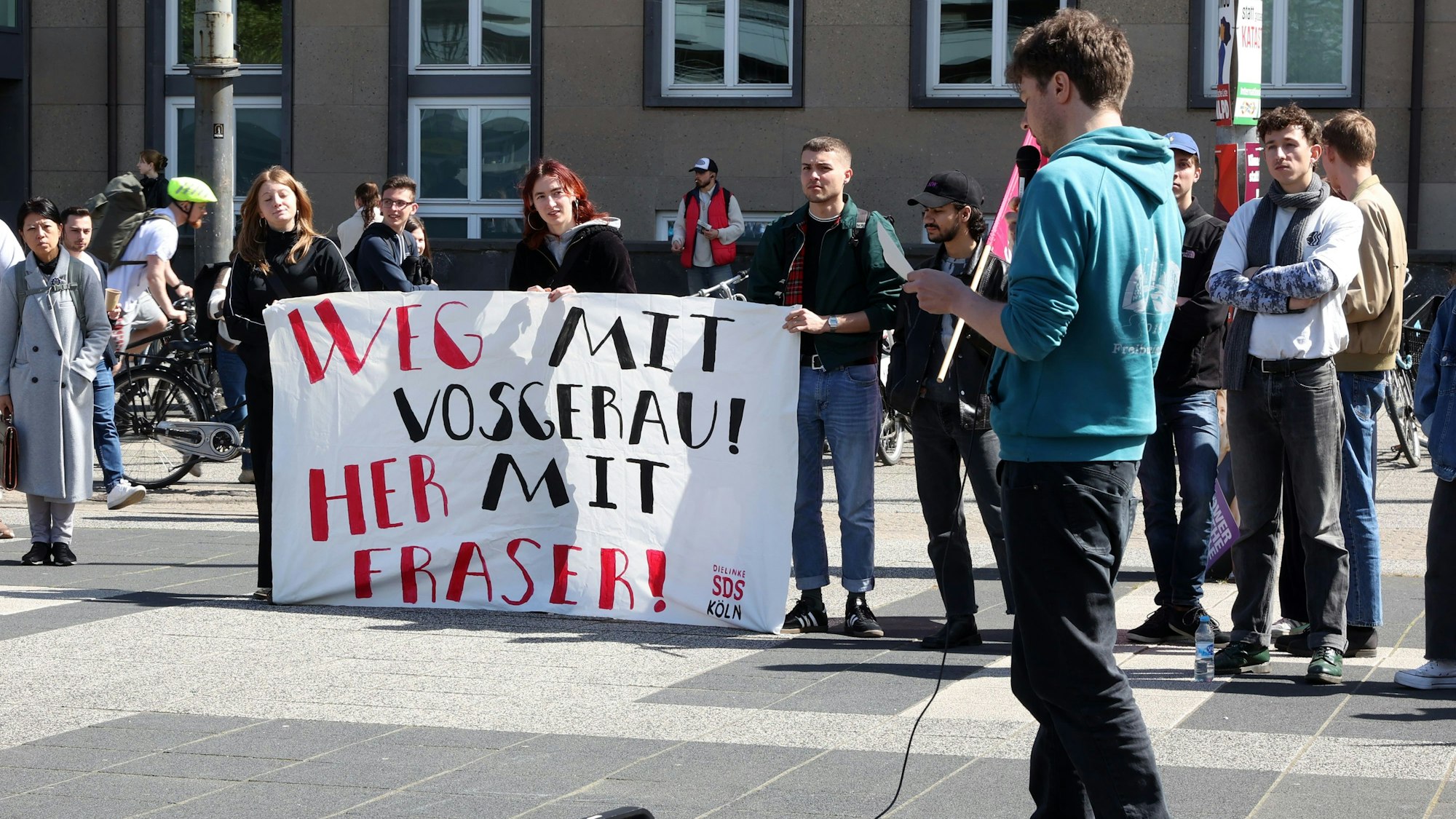 Studierende demonstrieren auf dem Albertus-Magnus-Platz. Auf einem Plakat steht: „Weg mit Vosgerau! Her mit Fraser!“
