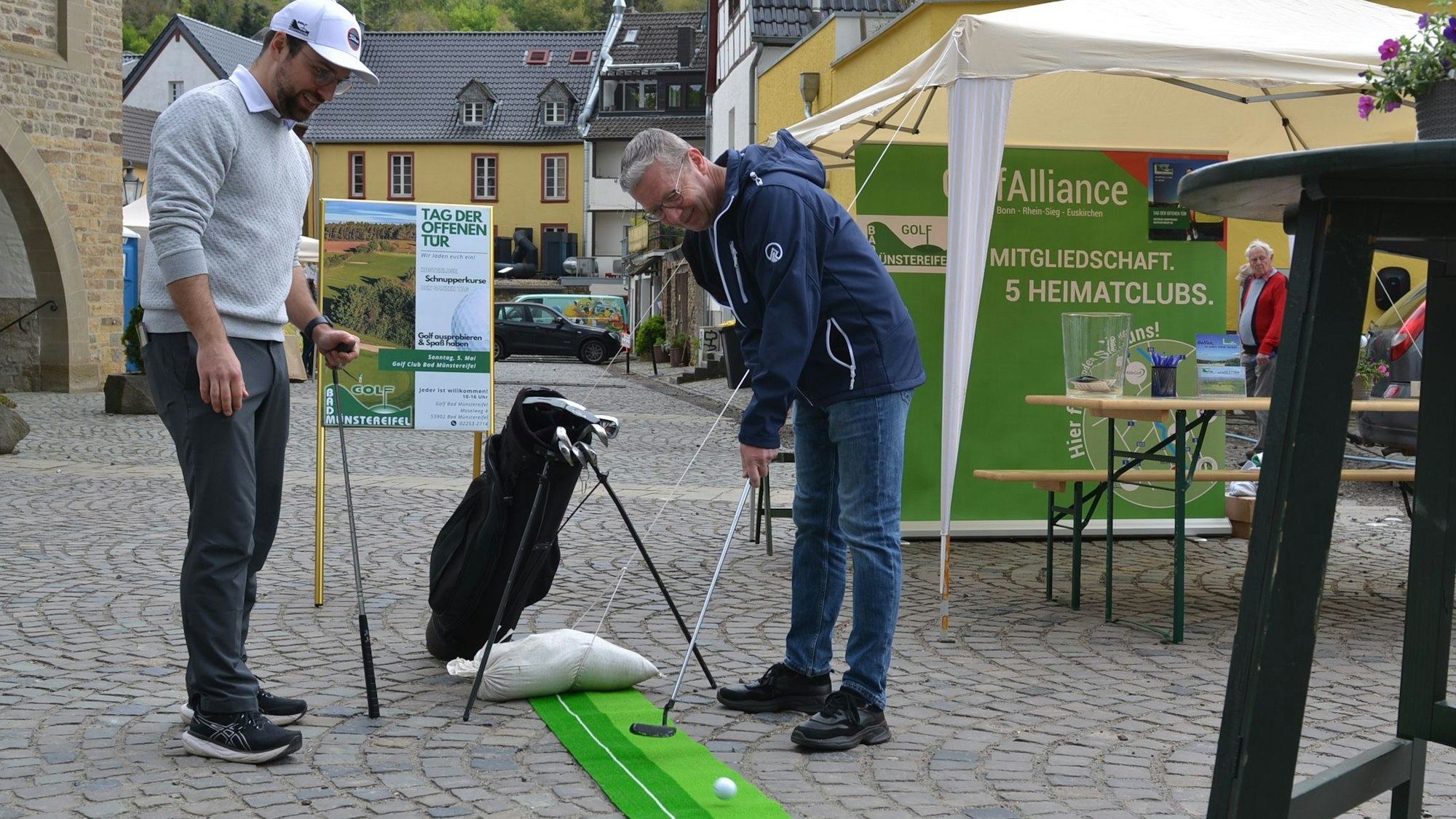 Ein Mann probiert einen Schlag auf einer kleinen Golfbahn, ein anderer schaut zu.