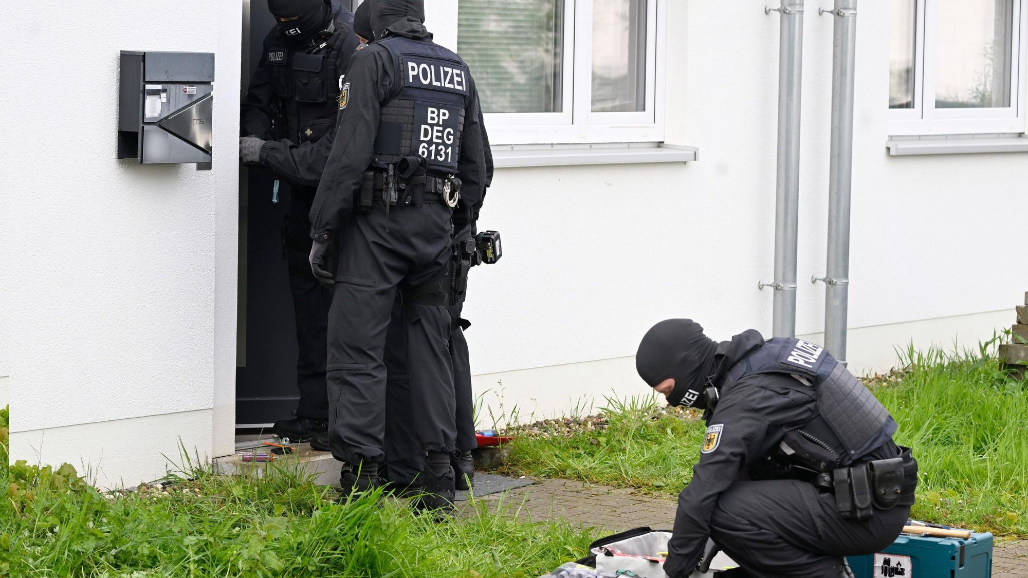 Das Bild zeigt maskierte Polizeibeamte vor einem Haus, das durchsucht wird.