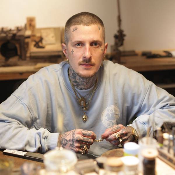 Ludwig Friedländer, Goldschmied und Schmuckdesigner aus Köln-Bayenthal sitzt im Pulli in seiner Werkstatt und hält ein goldenes Armband zwischen seinen Fingern.