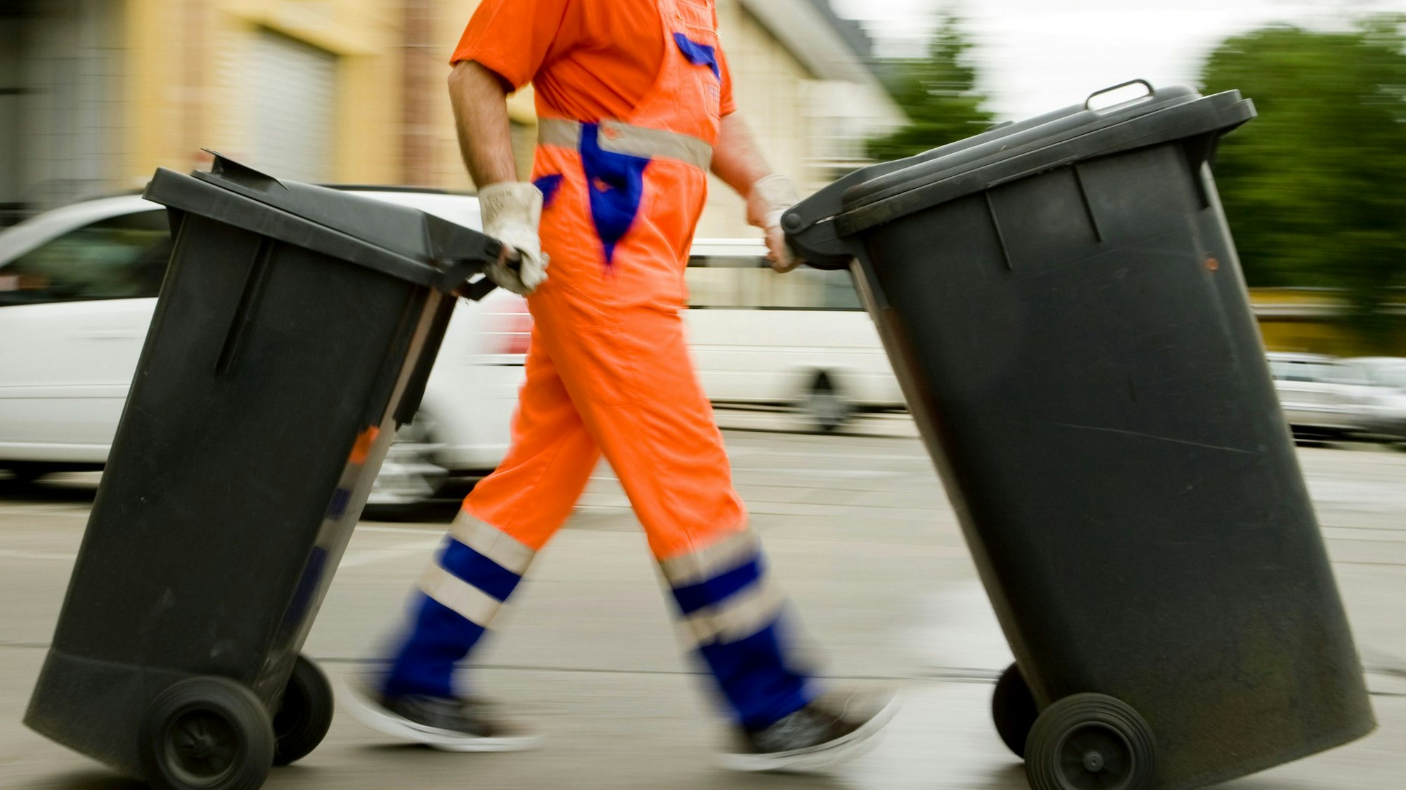Ein Müllmann schiebt Mülltonnen über die Straße.