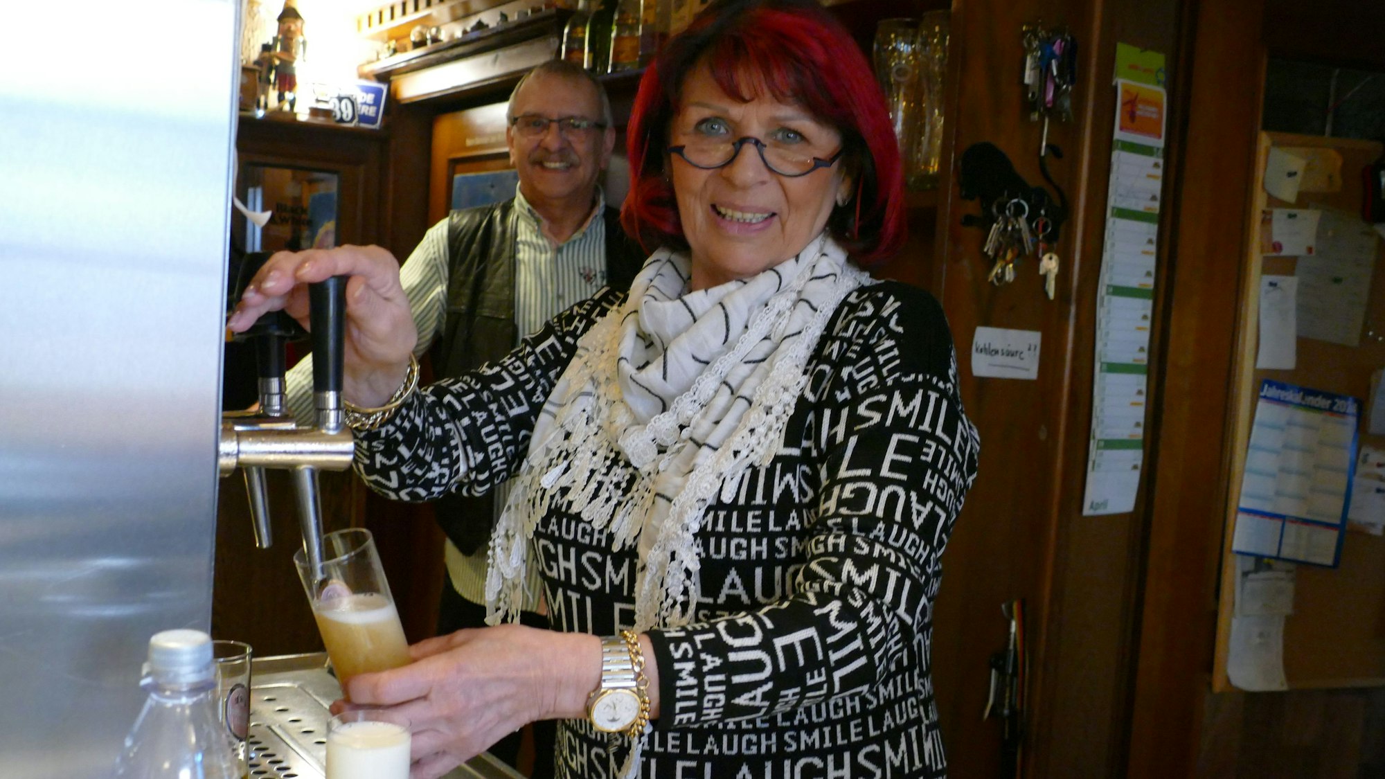 Ihren Gästen serviert Monika Adam Reissdorf Kölsch. Im Hintergrund steht ihr Mann Karl Heinz Schiffer, der ebenfalls hier arbeitet.