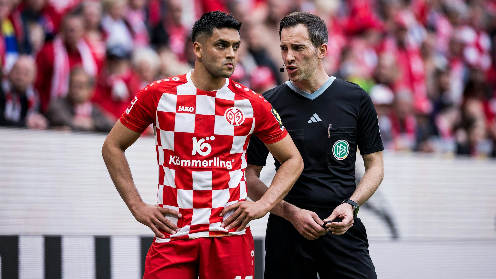 Nadiem Amiri und Schiedsrichter Benjamin Brand sprechen vor der Kölner Kurve nachdem der Spieler er bei einer Ecke mit Gegenständen beworfen wurde.