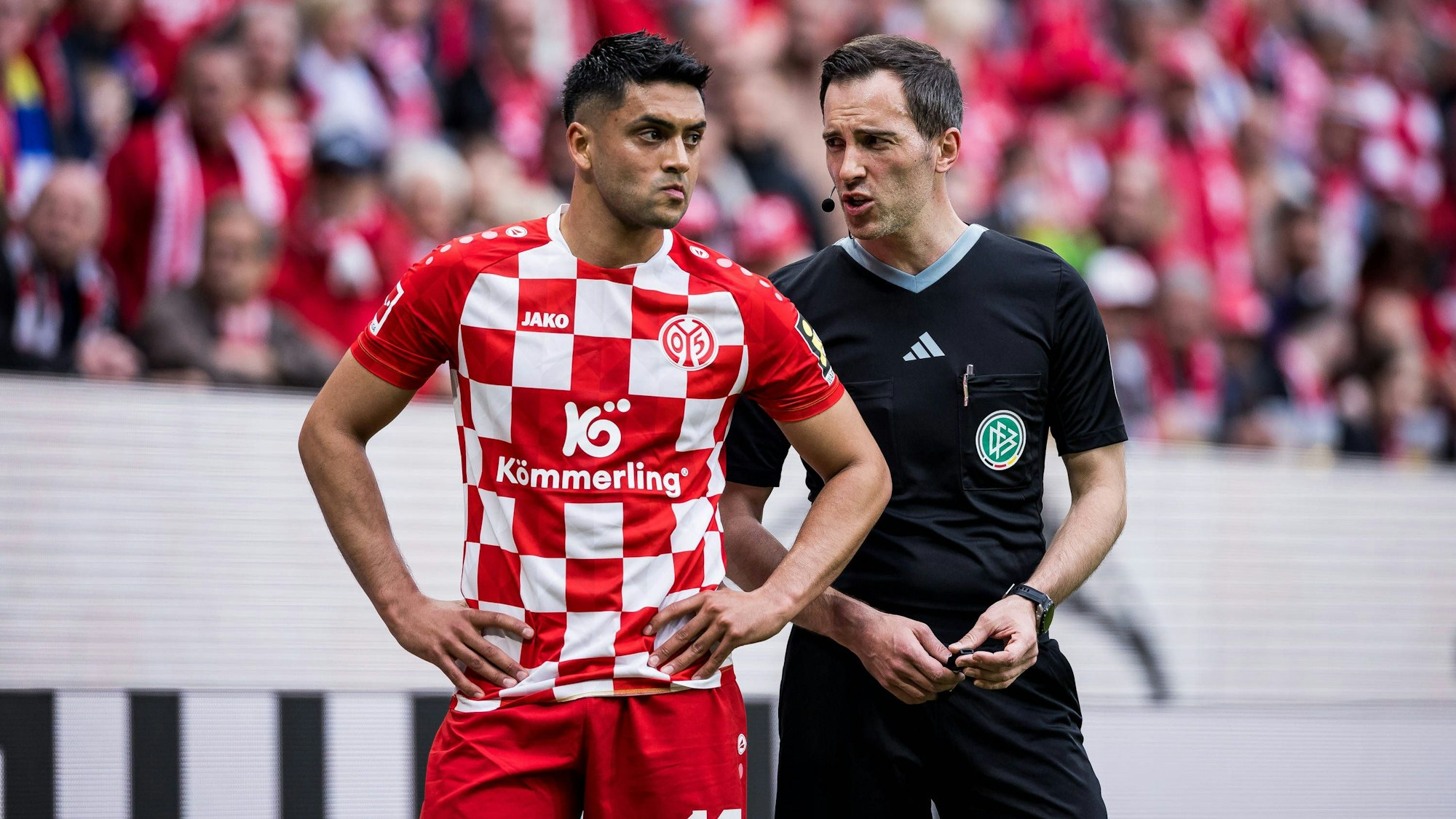 Nadiem Amiri und Schiedsrichter Benjamin Brand sprechen vor der Kölner Kurve nachdem der Spieler er bei einer Ecke mit Gegenständen beworfen wurde.