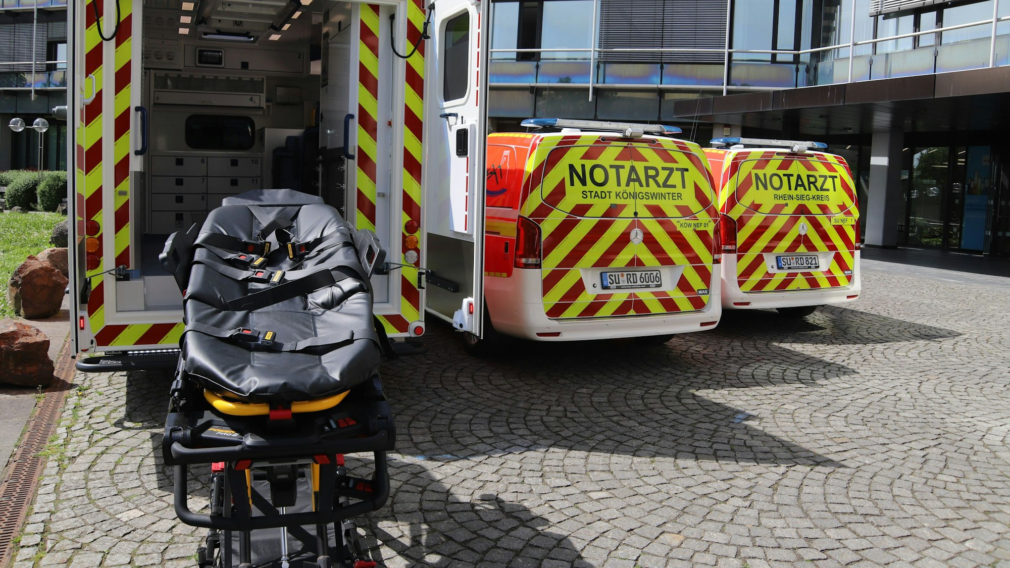 Die elektrohydraulische Fahrtrage steht hinter einem Rettungstransportwagen und neben zwei Notarzteinsatzfahrzeugen.