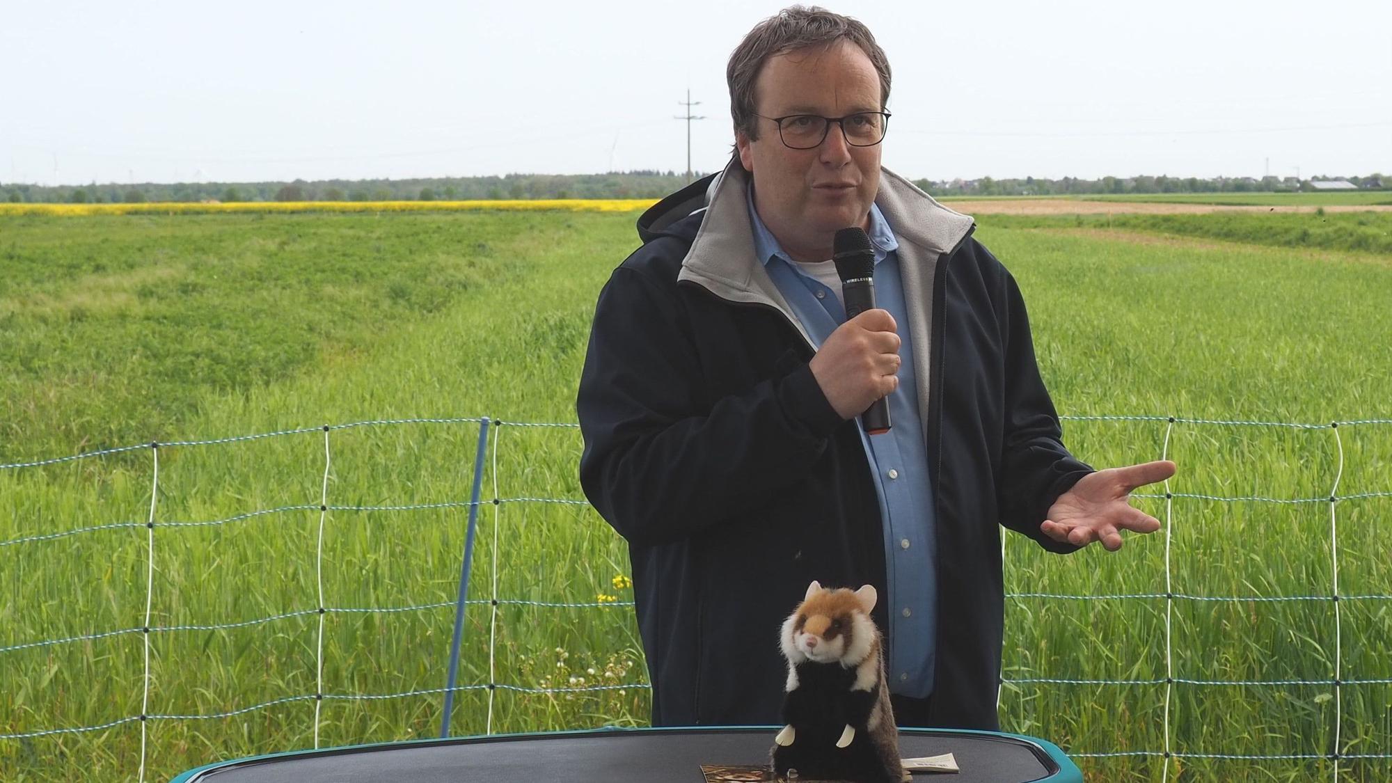 Minister Oliver Krischer spricht in ein Mikrofon. Vor ihm steht ein Plüschhamster.