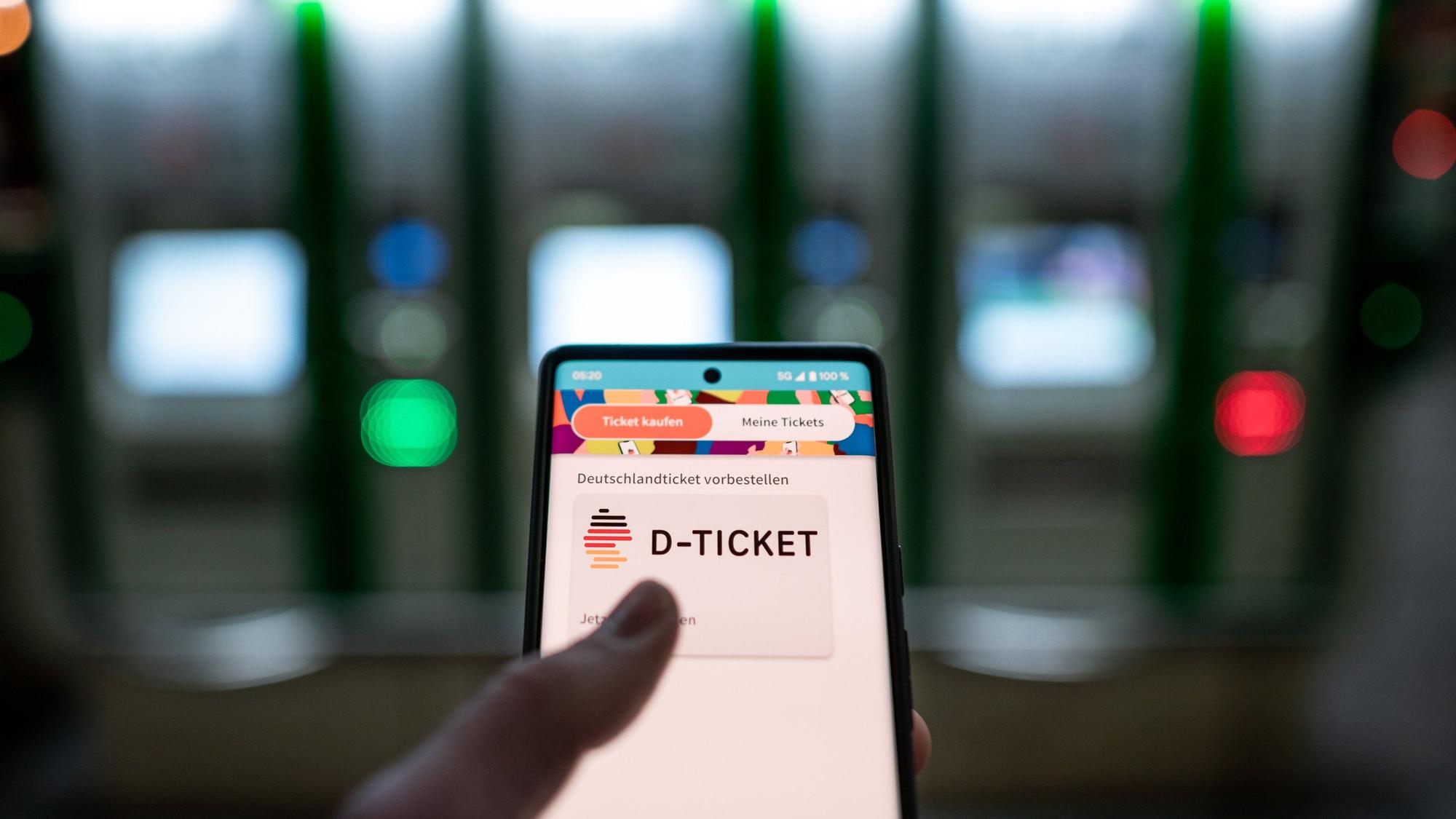 Ein Mann hält ein Mobiltelefon, auf dem das D-Ticket gekauft werden kann, vor Ticketautomaten am Hauptbahnhof in der Hand.