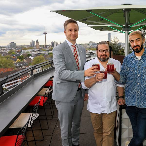 Drei Männer stehen mit Drinks in der Hand auf der Terrasse einer Rooftop-Bar.