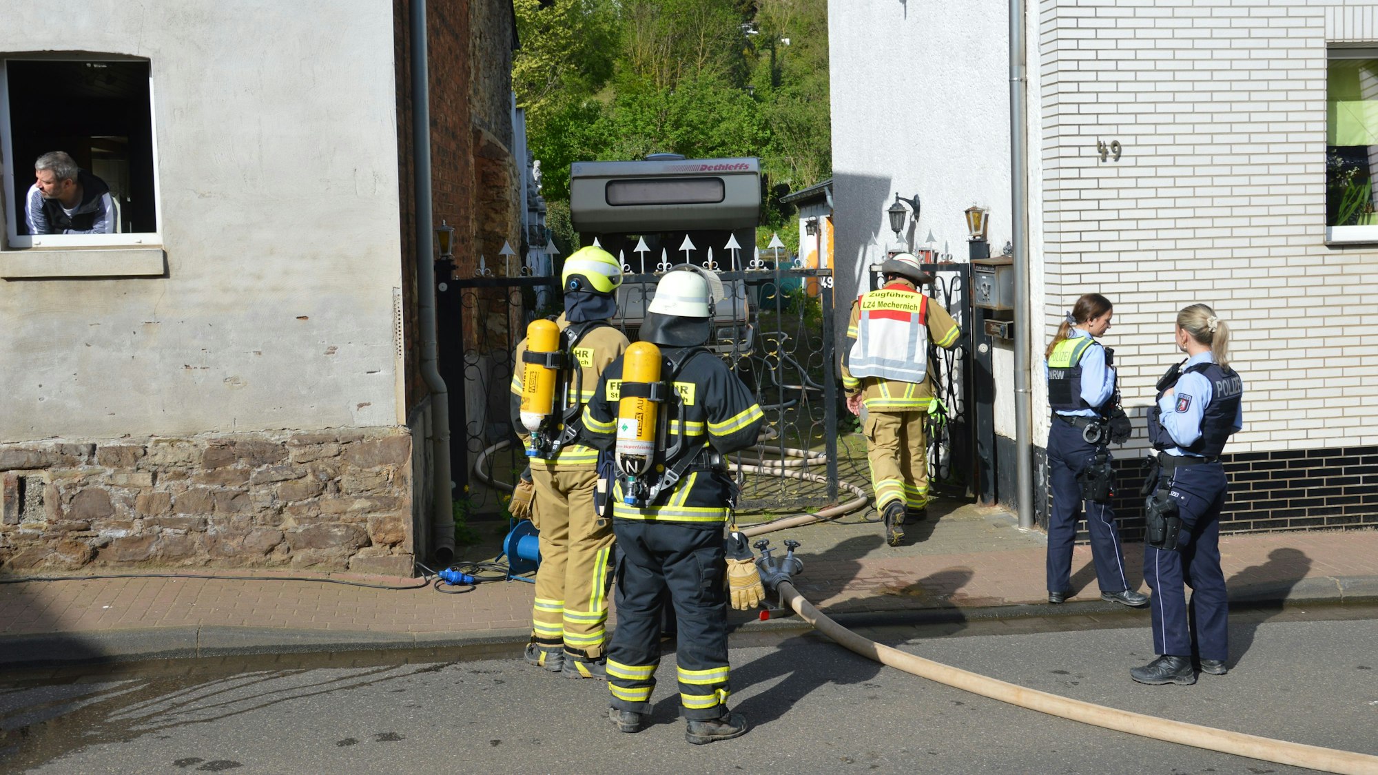 Feuerwehrleute und zwei Polizistinnen stehen vor dem Haus in der Hauserbachstraße.