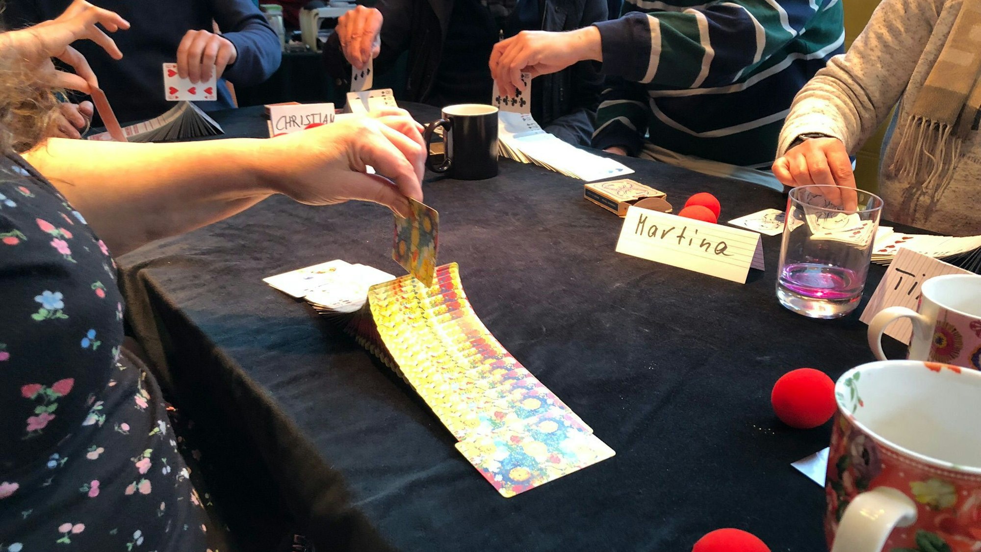 Nahaufnahme eines Tisches: Mehrere Hände mischen ein Kartenspiel.