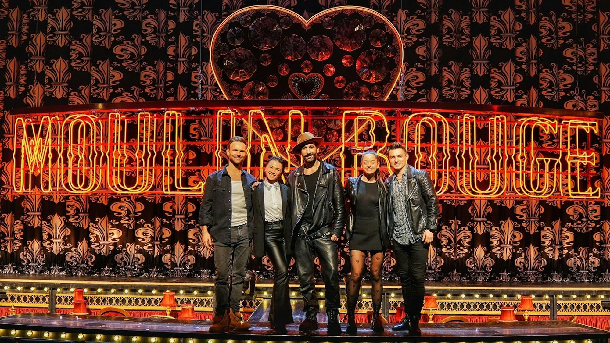 Fünf Personen stehen auf der Bühne vor einem Vorhang und dem Schriftzug "Moulin Rouge"