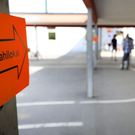 Eingang zu einem Wahllokal. Ein rotes Schild mit einem Pfeil darauf weist in die Richtung.