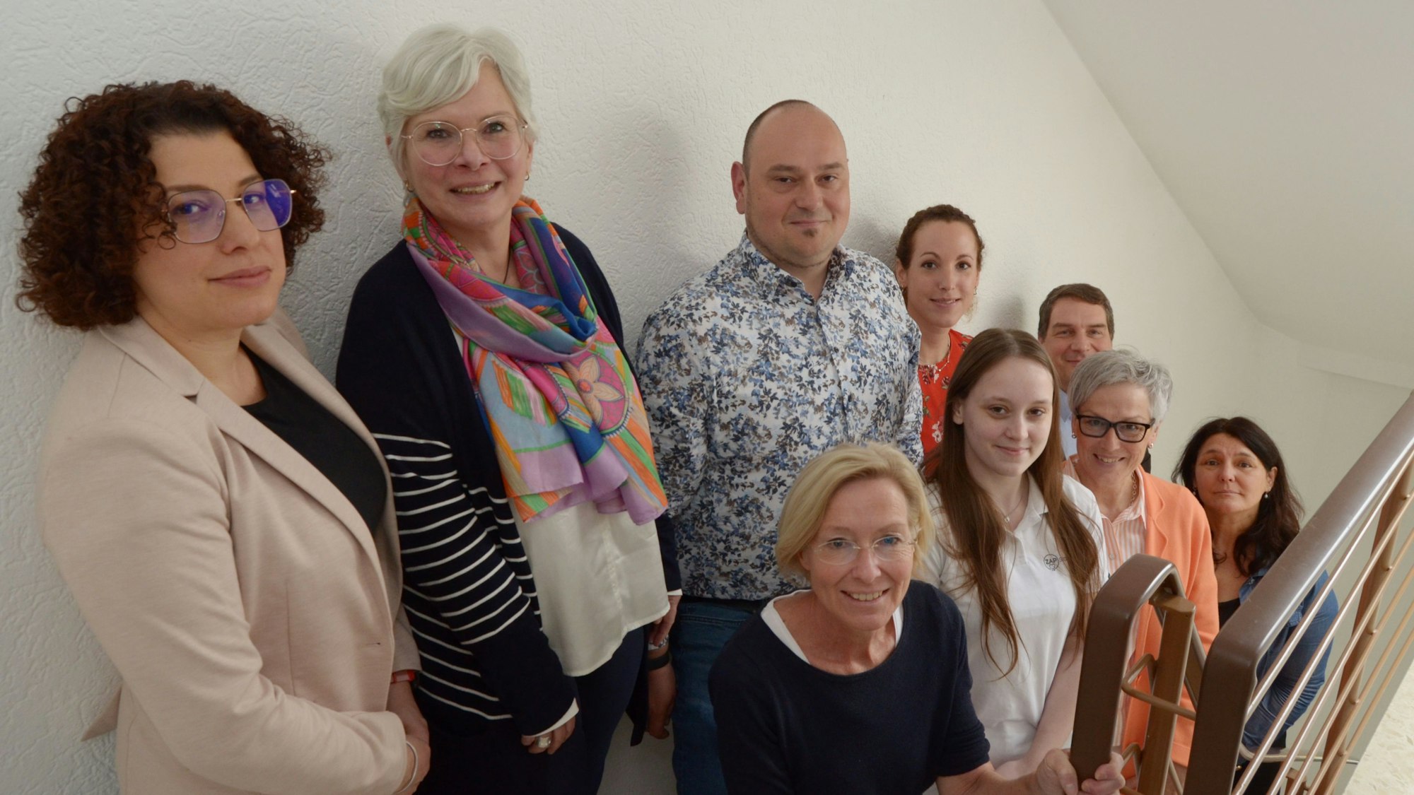 Neun Frauen und Männer haben sich zu einem Gruppenbild aufgestellt.