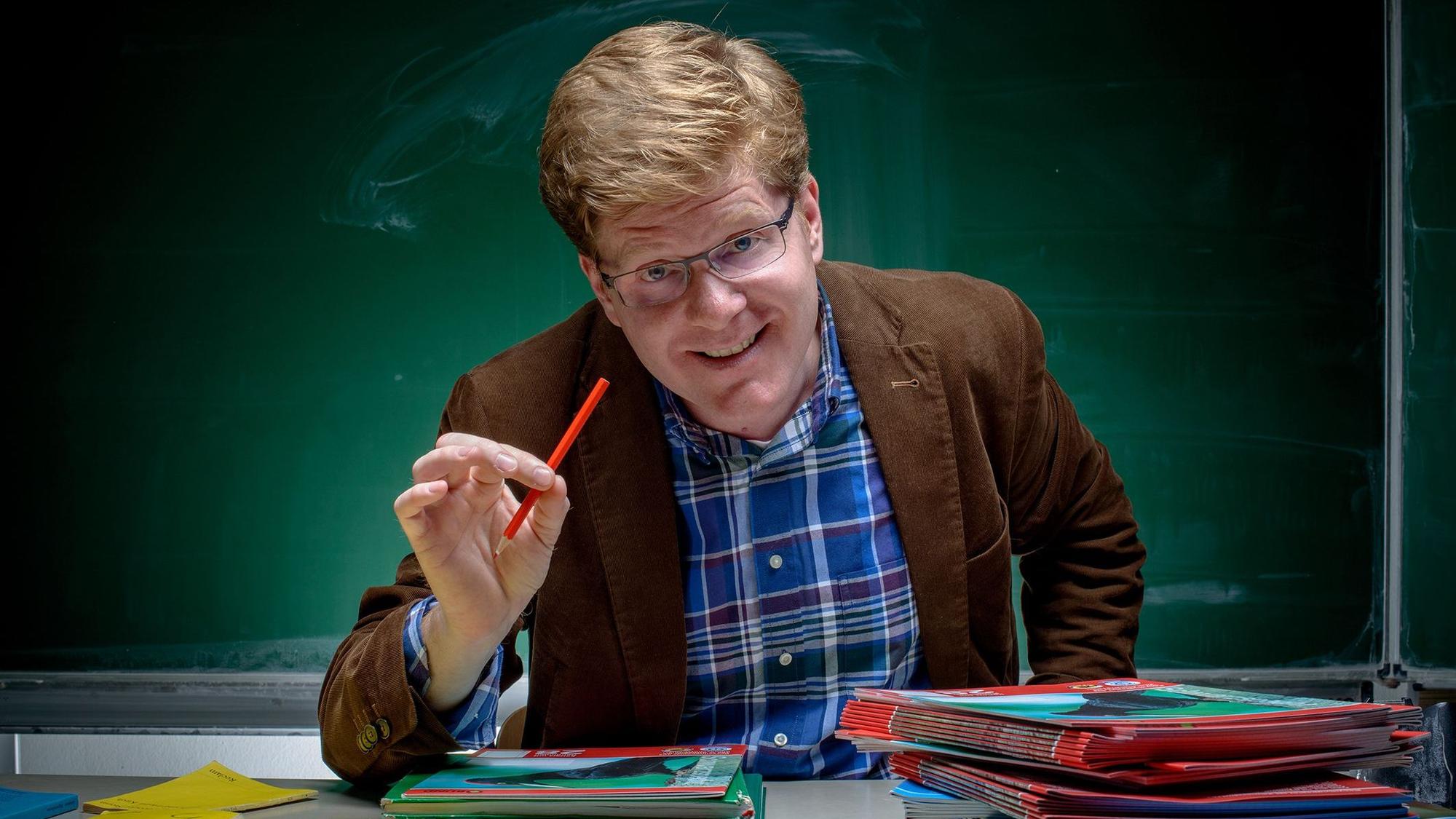 Ein Mann sitzt an einem Lehrerpult.