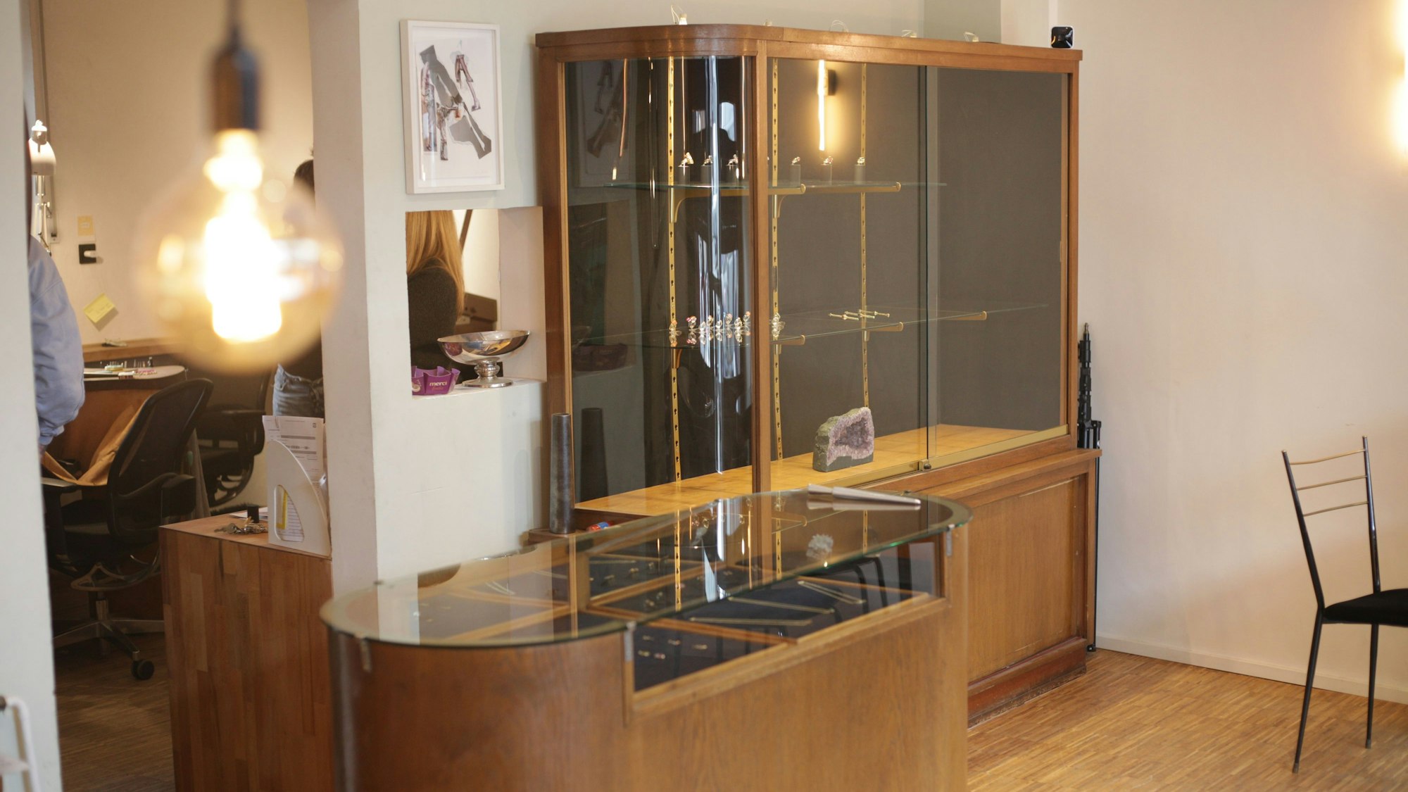 Zwei Holzvitrinen mit Glasauslage stehen im Verkaufsraum der Goldschmiede in Köln-Bayenthal. Links ist ein Wanddurchbruch der in die Werkstatt führt, wo die Schmuckstücke gefertigt werden.