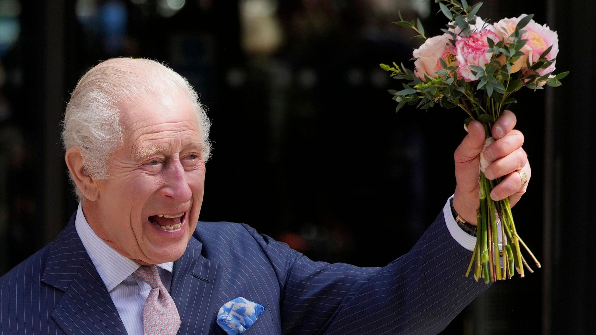 König Charles winkt mit Blumen.