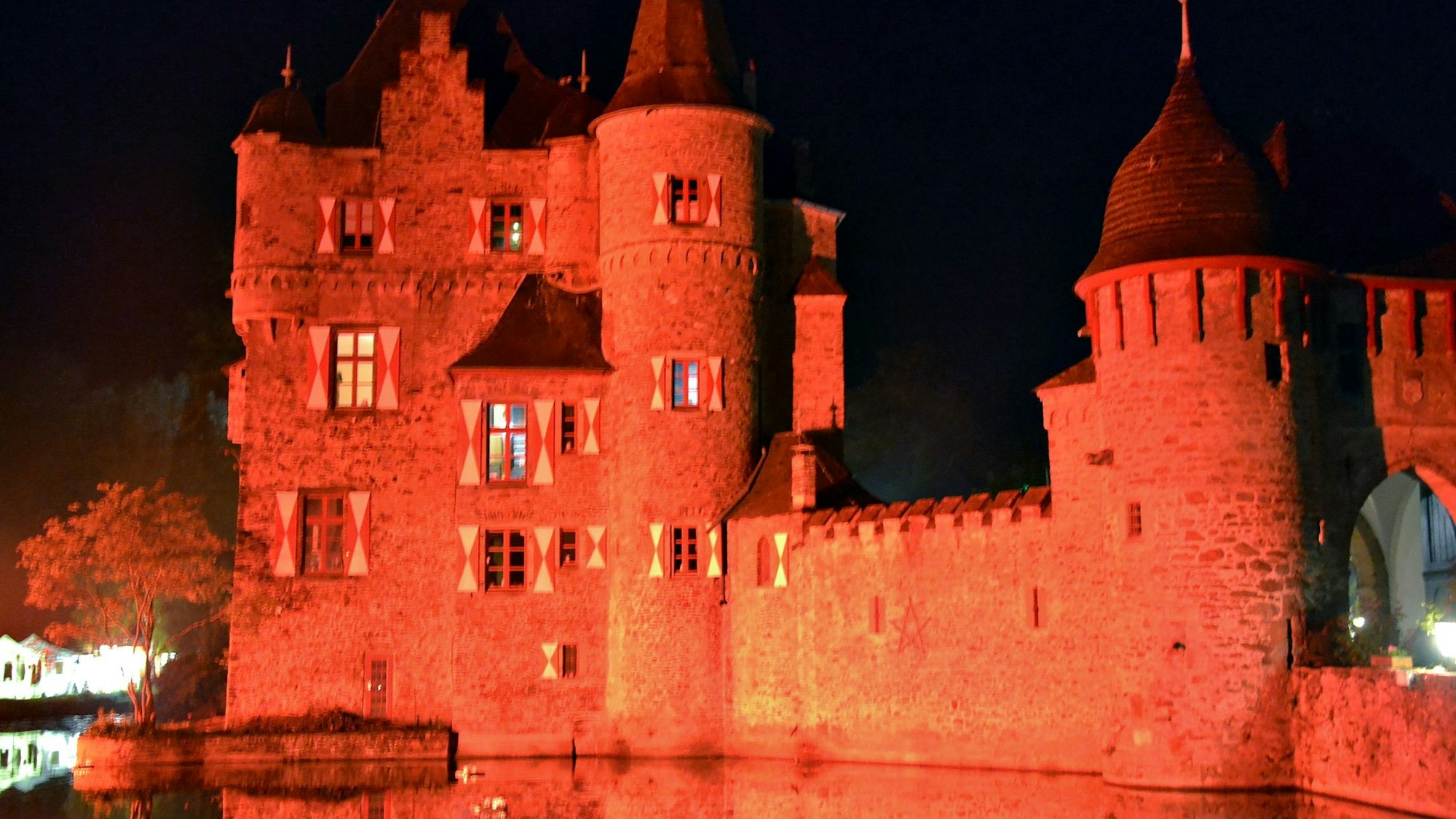Burg Satzvey ist in rotes Licht getaucht, im Vordergrund der mit Wasser gefüllte Burggraben.