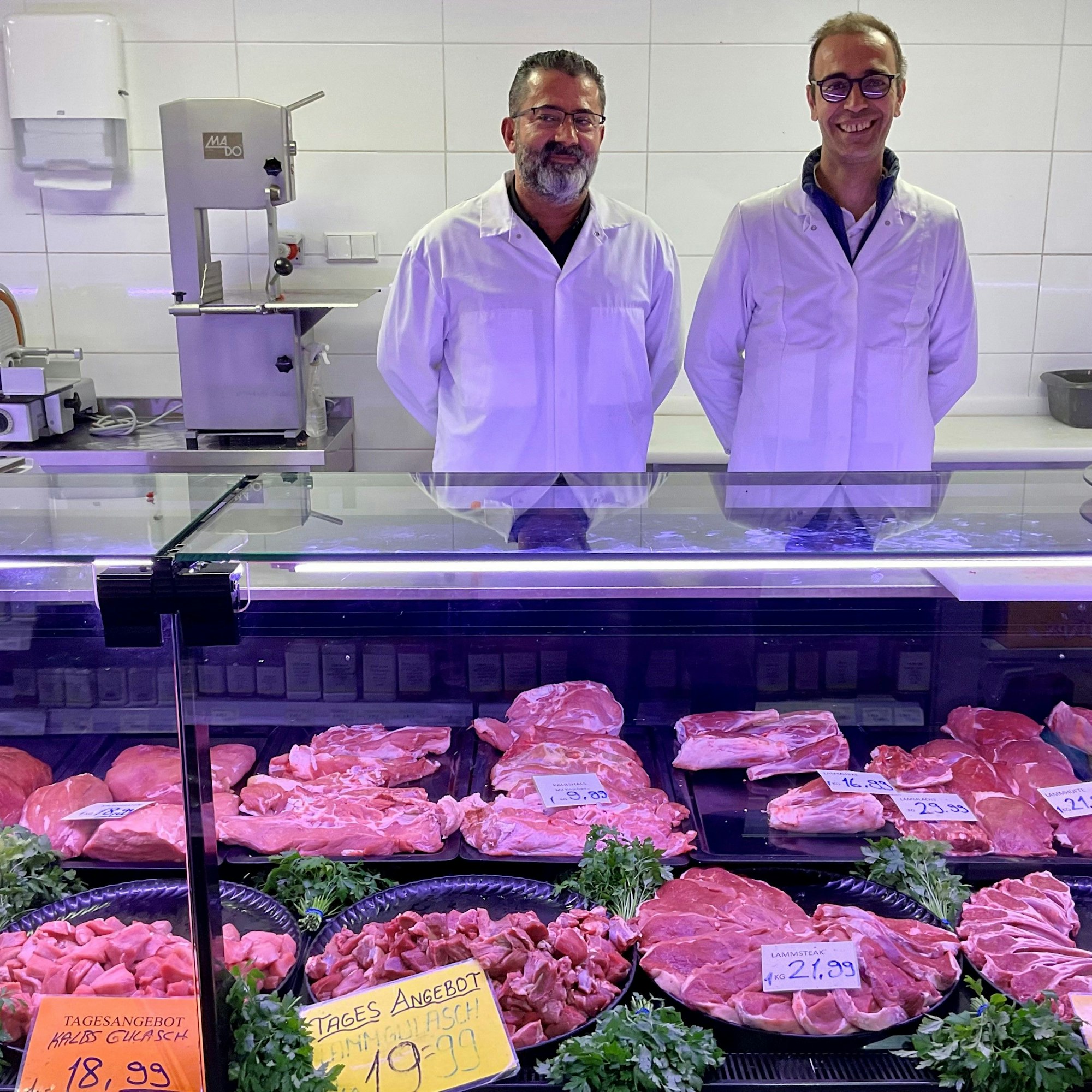 Zwei Männer im weißen Kittel hinter einer Fleischtheke