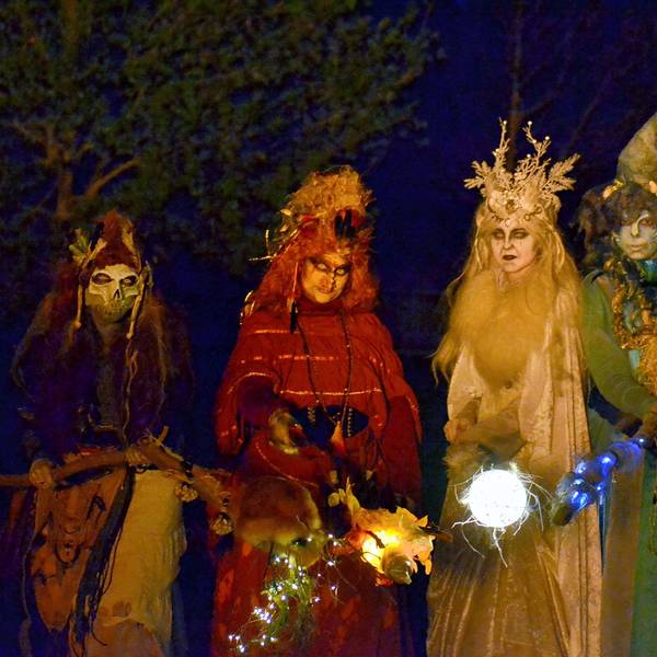 Vier farbenfroh kostümierte Hexen mit leuchtenden Fackeln in der Dunkelheit.