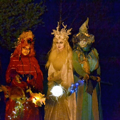 Vier farbenfroh kostümierte Hexen mit leuchtenden Fackeln in der Dunkelheit.