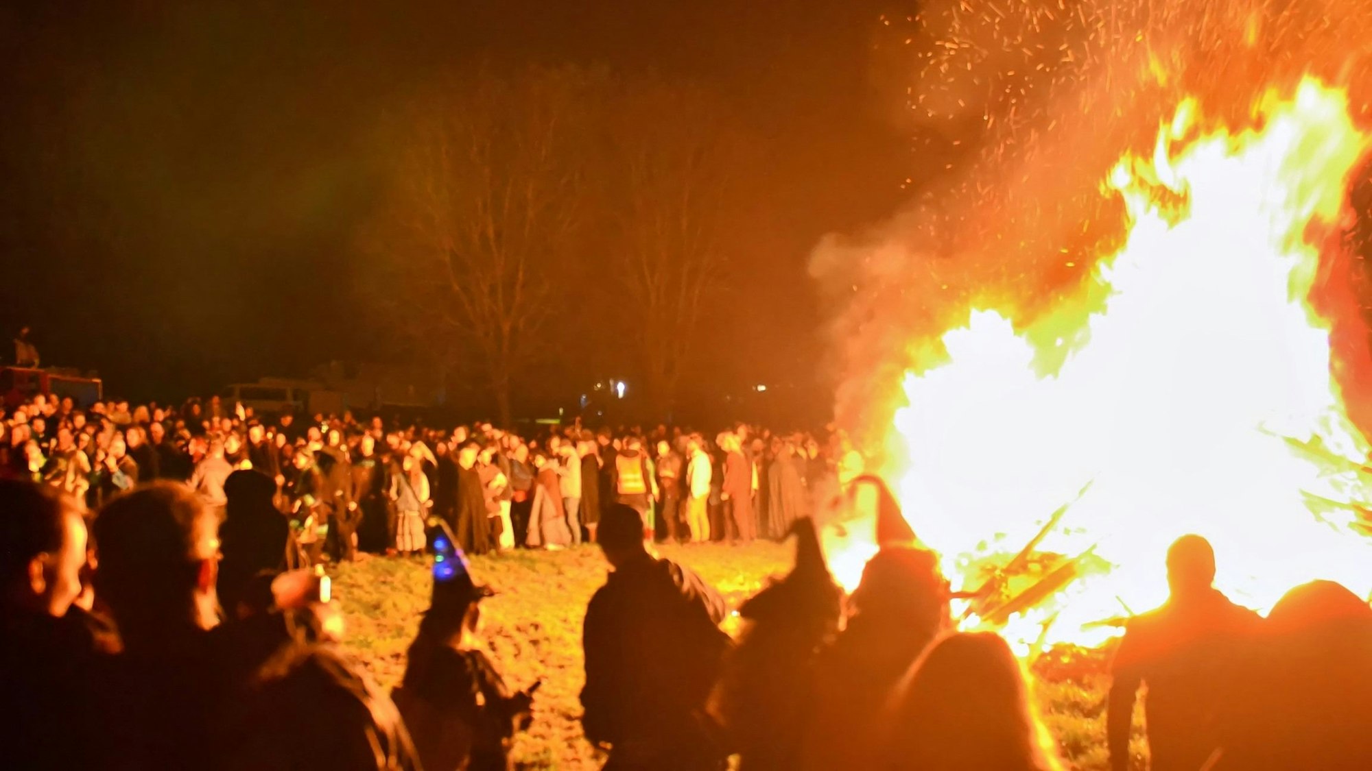 Hoch lodern die Flammen des Maifeuers auf Burg Satzvey, um das sich viele Zuschauer versammelt haben.