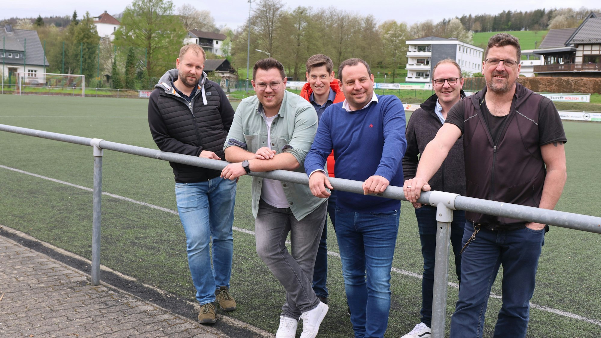 Sechs Männer stehen am Spielfeldrand des Kunstrasenplatzes.