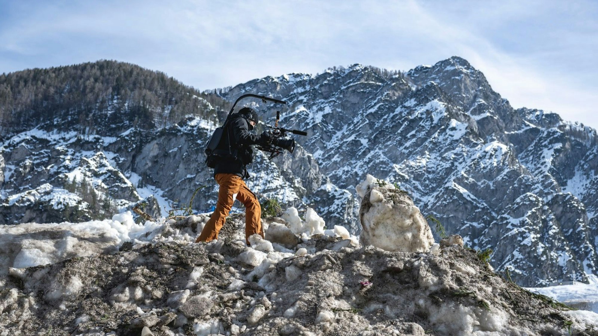 Eine Kamerafrau läuft über einen Haufen Schnee in den Bergen.