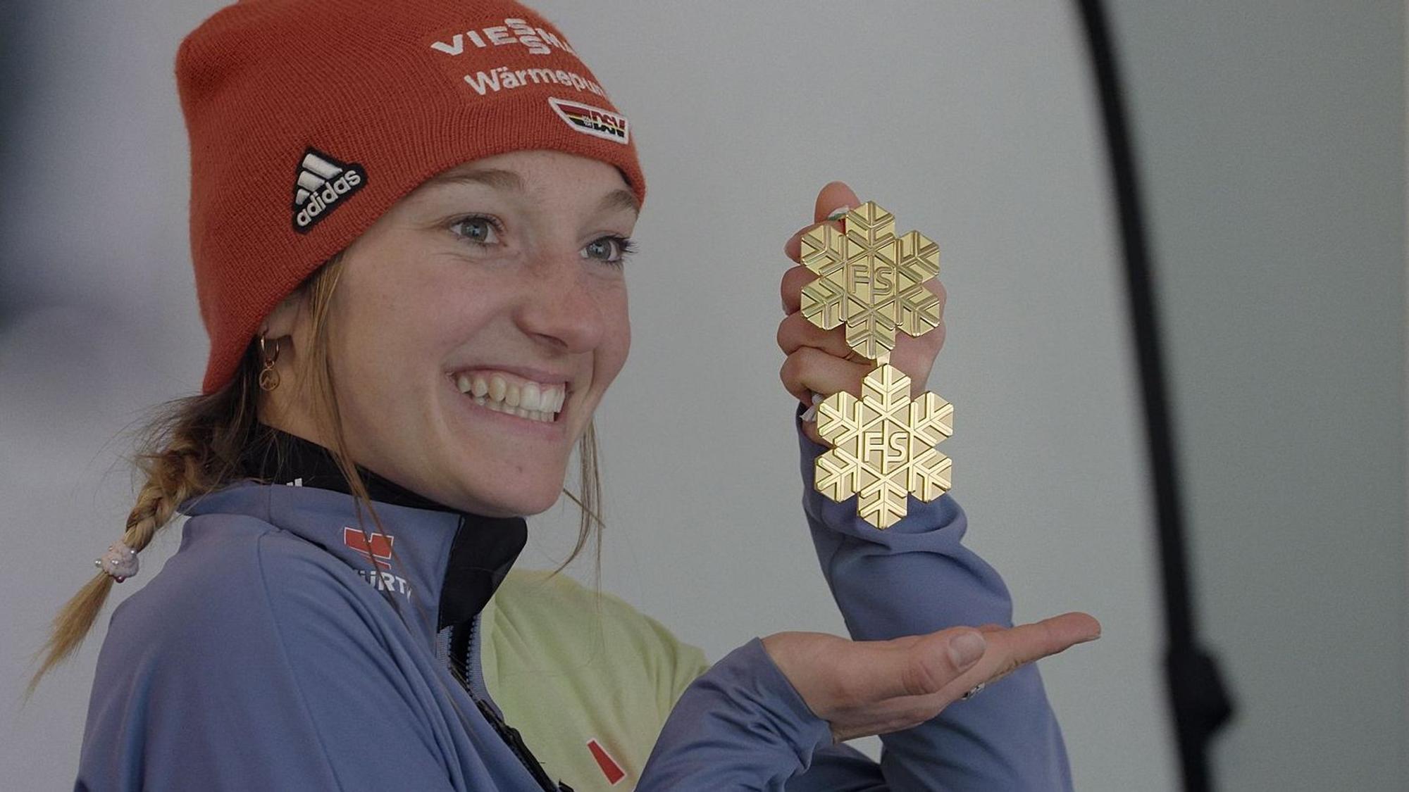 Katharina Schmid hält eine Medaille in die Luft.