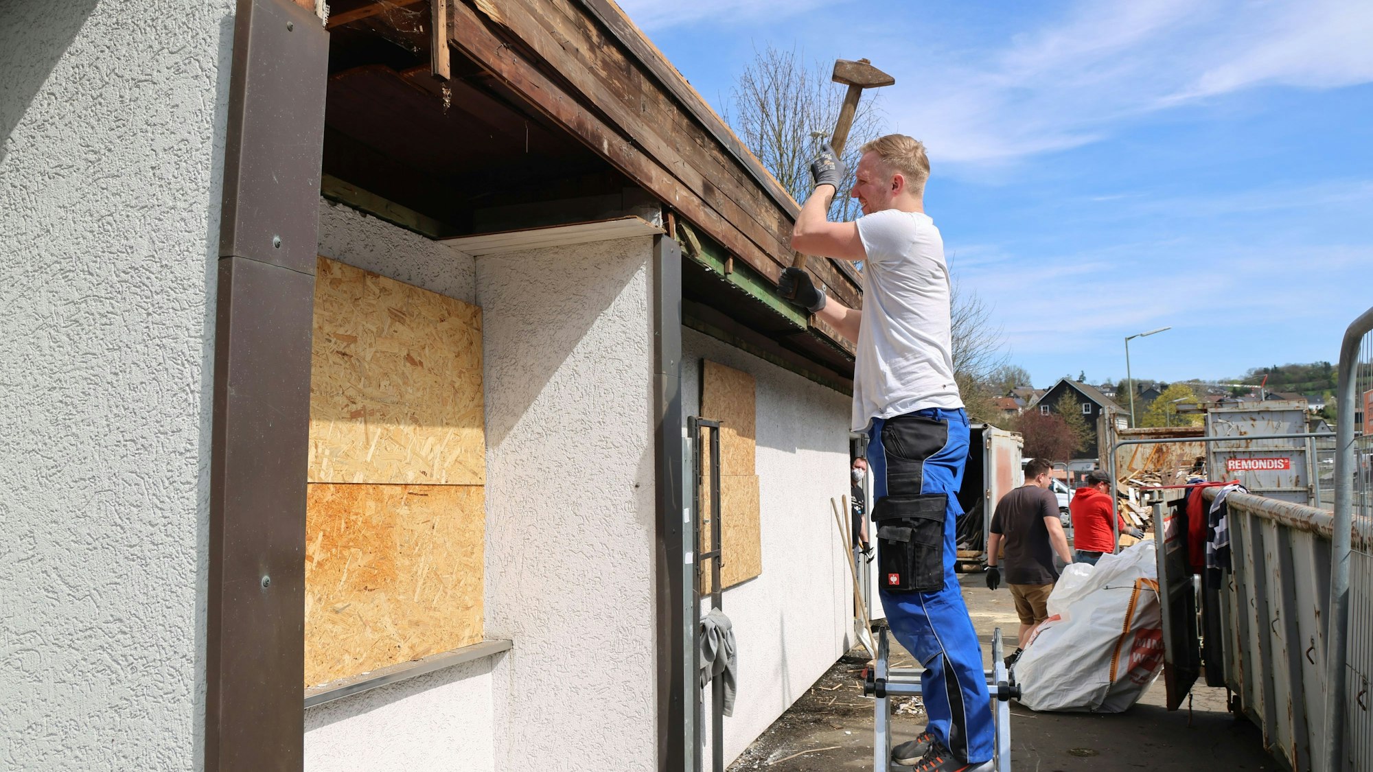 Ein Mann steht auf einer kleinen Leiter und schlägt mit einem großen Hammer aus das Gebäude.