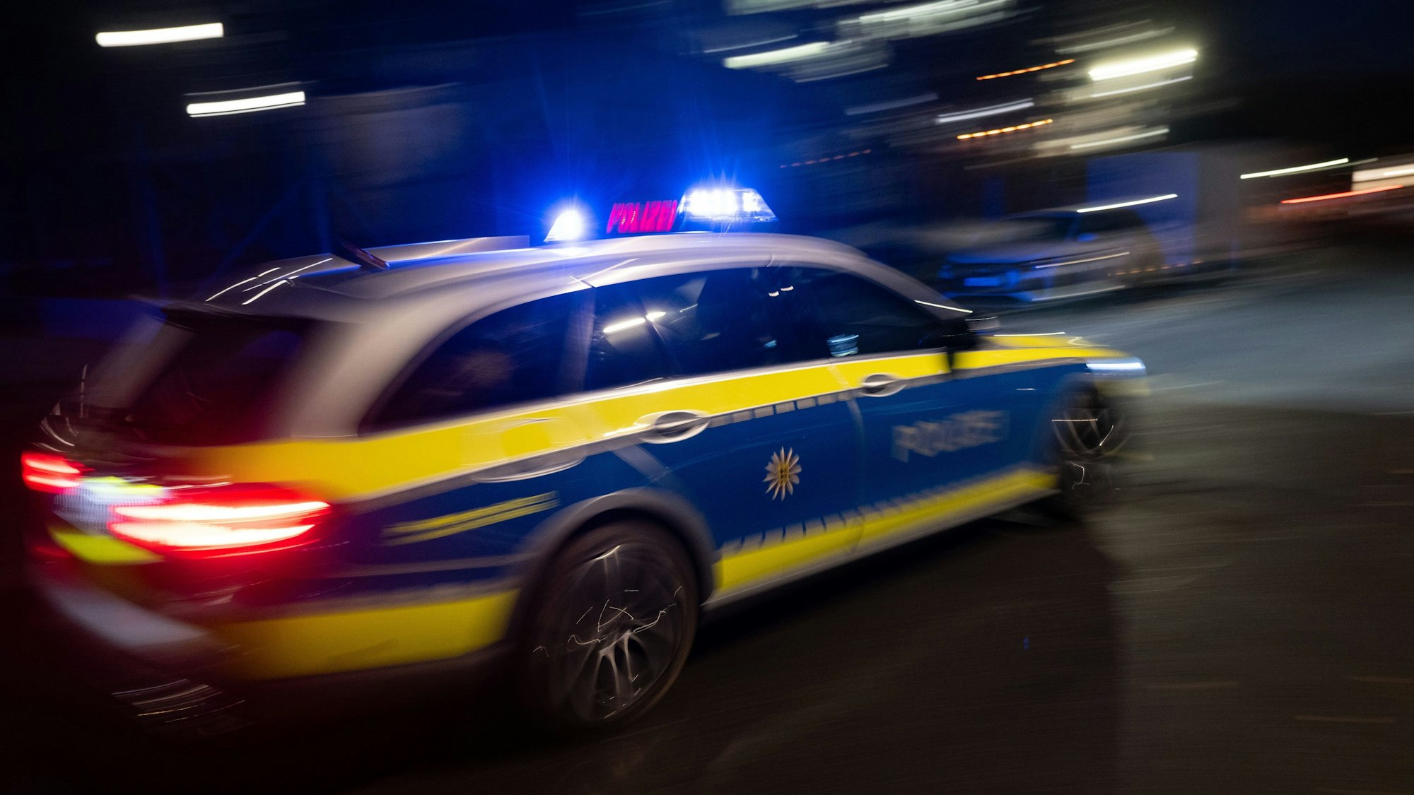 Ein Polizeifahrzeug fährt im Rahmen mit Blaulicht an einem Gebäude vorbei.