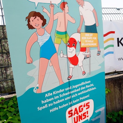 Am Zaun des Kölner Agrippa-Bads hängt das Plakat der „Ich sag’s!“-Kampagne zum Schutz vor sexualisierter Gewalt im Schwimmbad. Daneben hängt ein Bannder der Köln-Bäder.