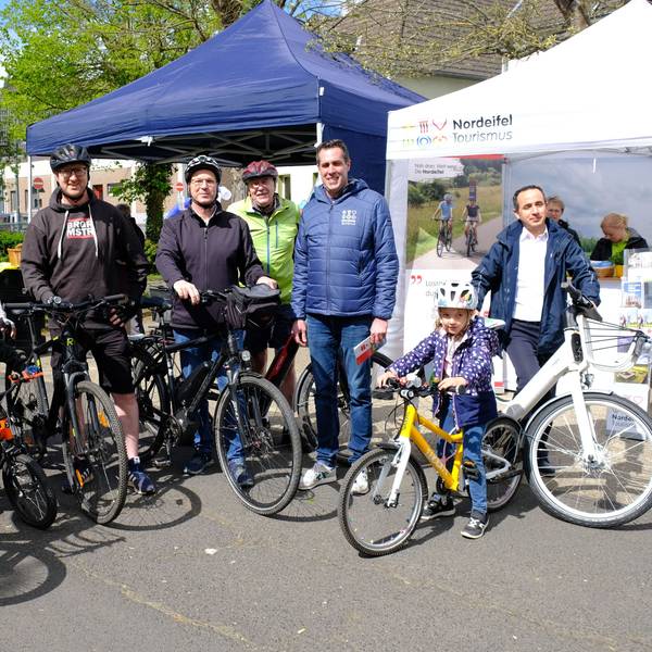 Mehrere Radfahrer, darunter zwei Kinder, stehen mit ihren Fahrrädern in Schleiden vor zwei Zelt-Pavillons.
