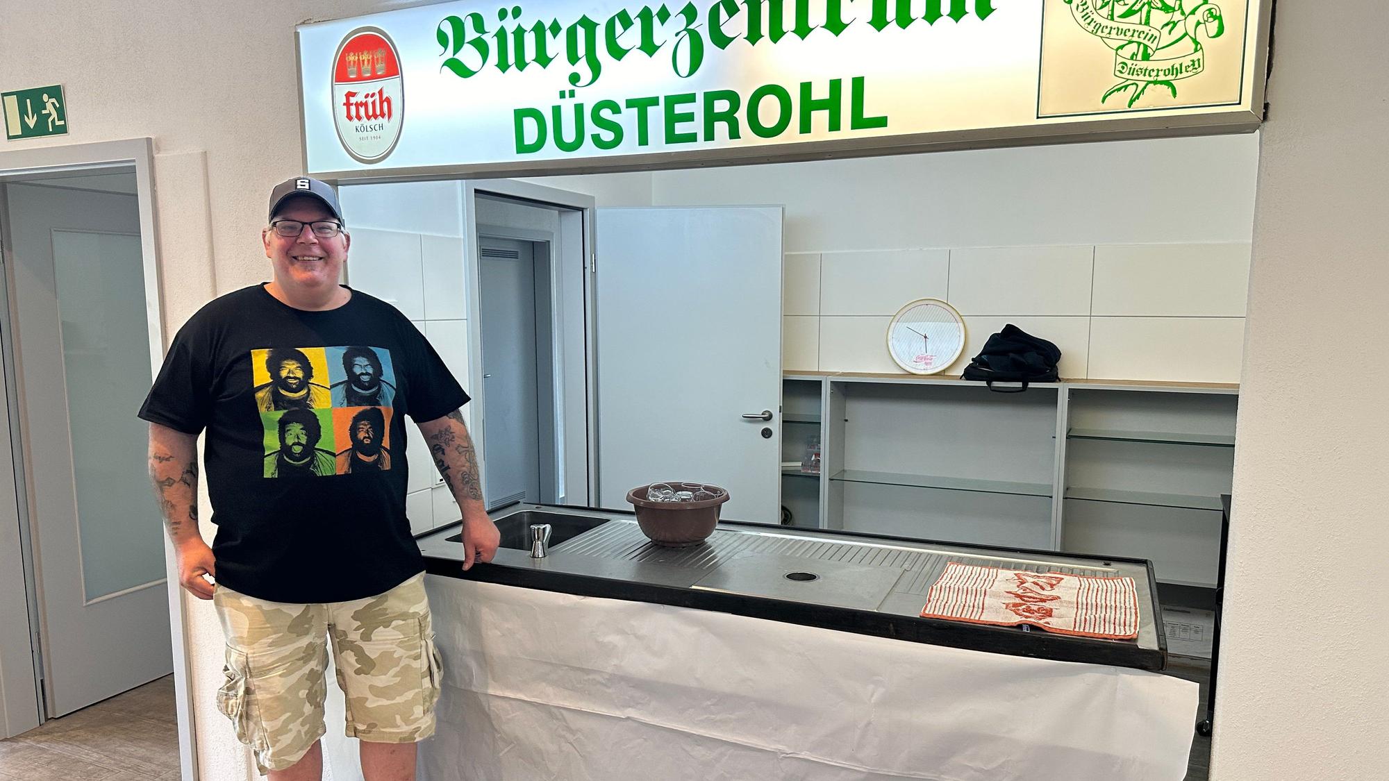 Sascha Scheider vom Bürgerverein Düsterohl steht vor einer niedrigen Theke, darüber hängt eine Leuchtreklame.