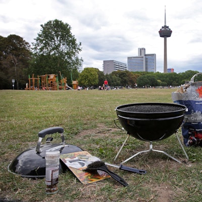 Auf einer Wiese steht ein Grill und ein Sack Kohle.
