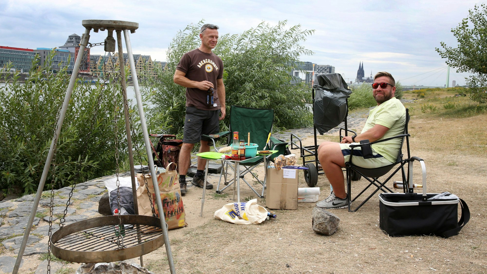 Zwei Männer grillen am Ufer eines Flusses.
