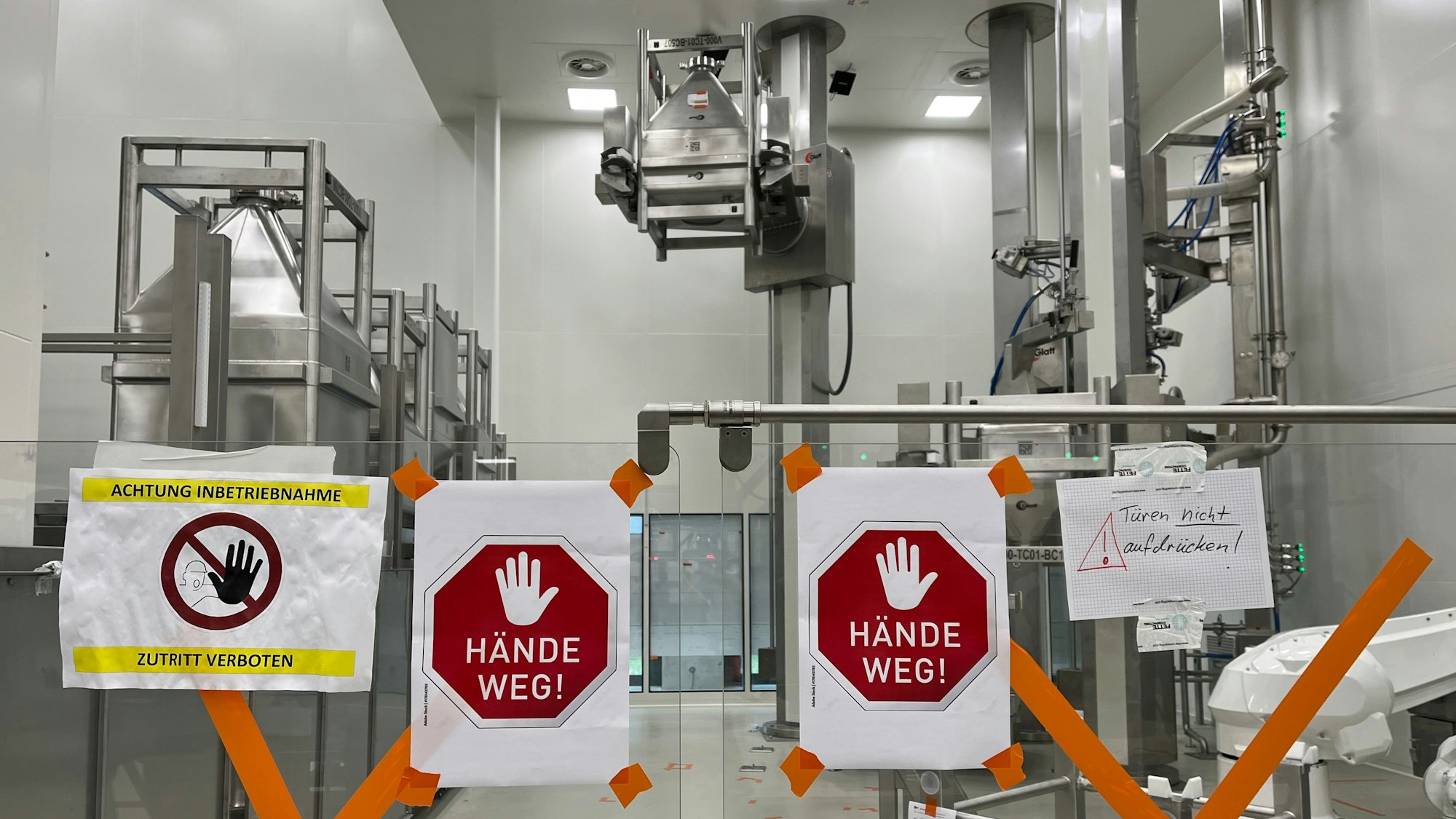 Blick auf einen Teil der neuen Tablettenproduktion von Bayer am 3. Mai 2024. Im Vordergrund hängen Schilder mit der Aufschrift „Hände weg“.