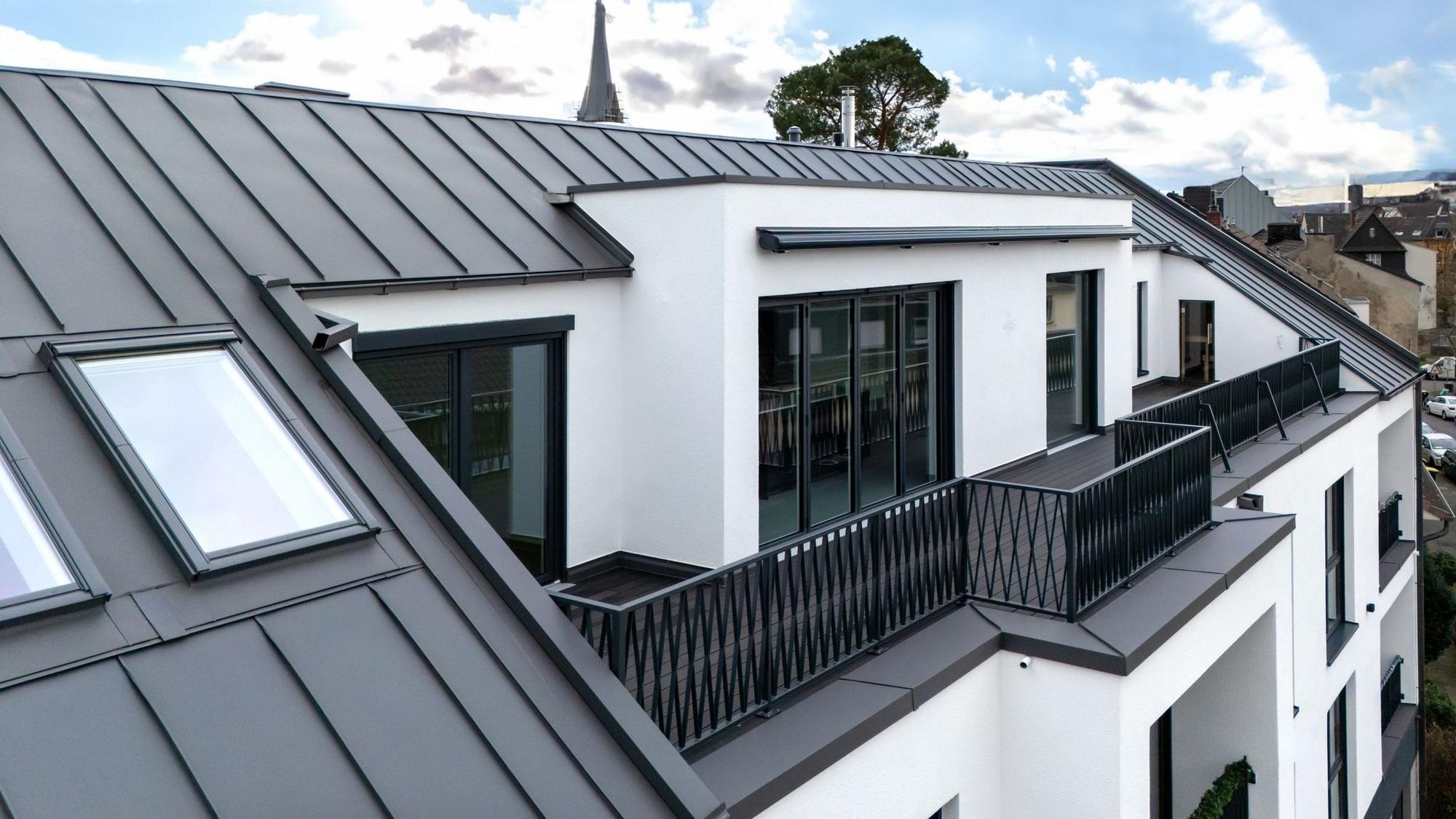 Außenansicht des Dachgeschosses, in dem sich das Penthouse befindet. Zu sehen ist die mit dunklem Boden ausgelegte Dachterrasse der Wohnung.