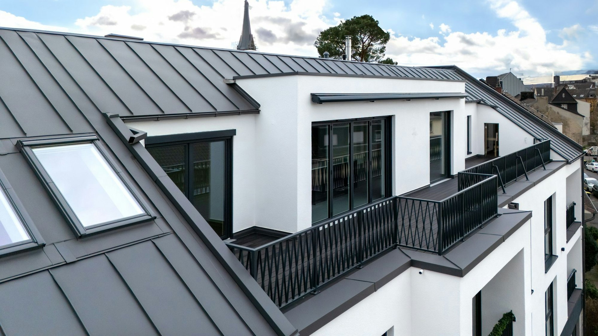 Außenansicht des Dachgeschosses, in dem sich das Penthouse befindet. Zu sehen ist die mit dunklem Boden ausgelegte Dachterrasse der Wohnung.