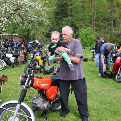 Ein älterer Herr zeigt einem kleinen Kind ein Motorrad.