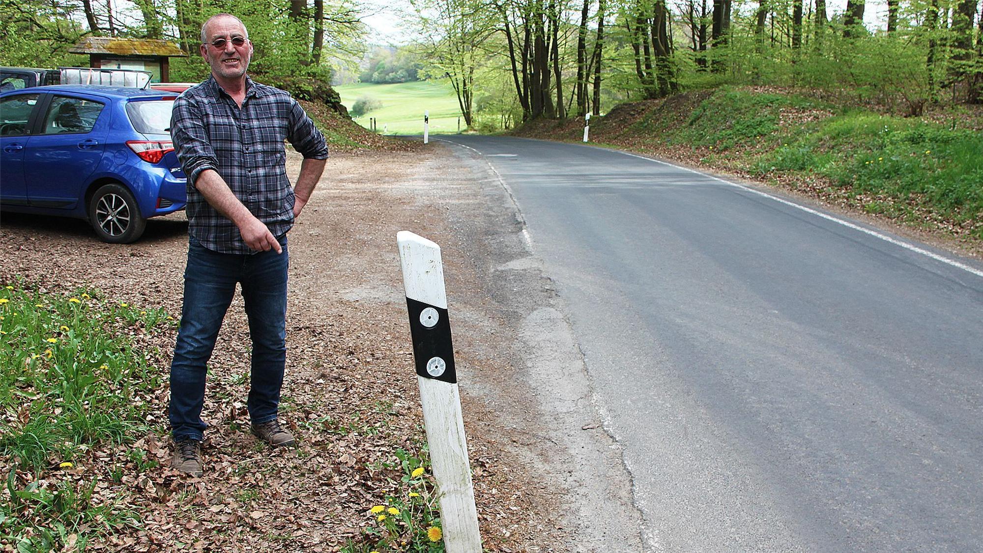 Ein Mann steht an einem Leitpfosten an einer Straße.