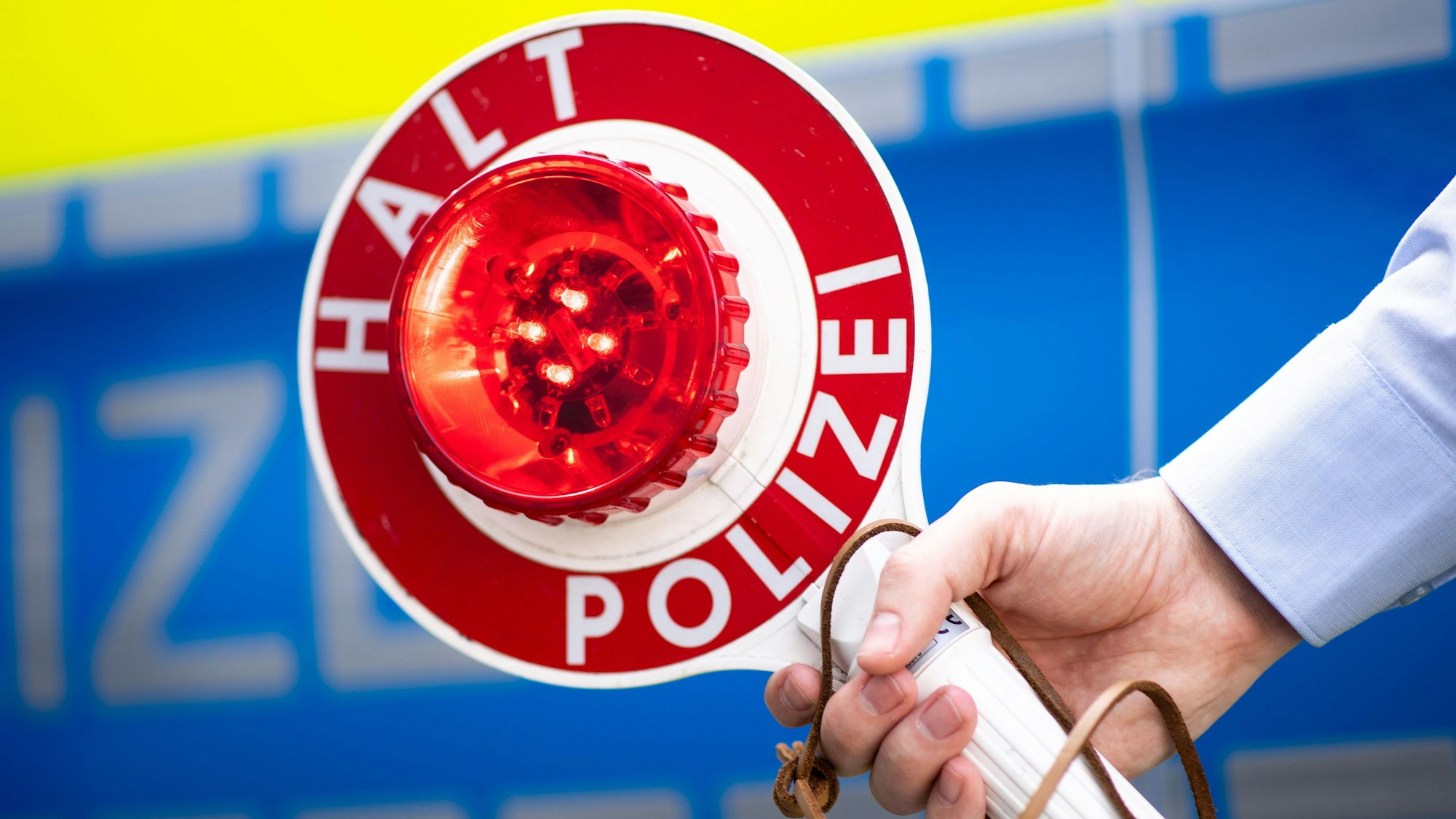 Ein Polizist hält eine Polizeikelle mit der Aufschrift „Halt Polizei“ in der Hand.