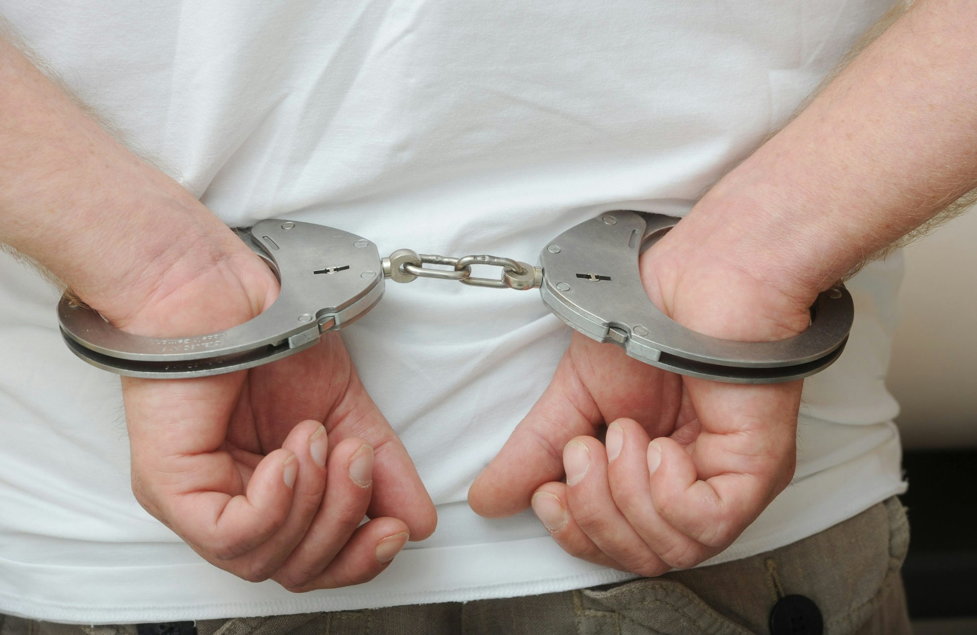 Zwei männliche Hände sind in Polizeihandschellen gefesselt.