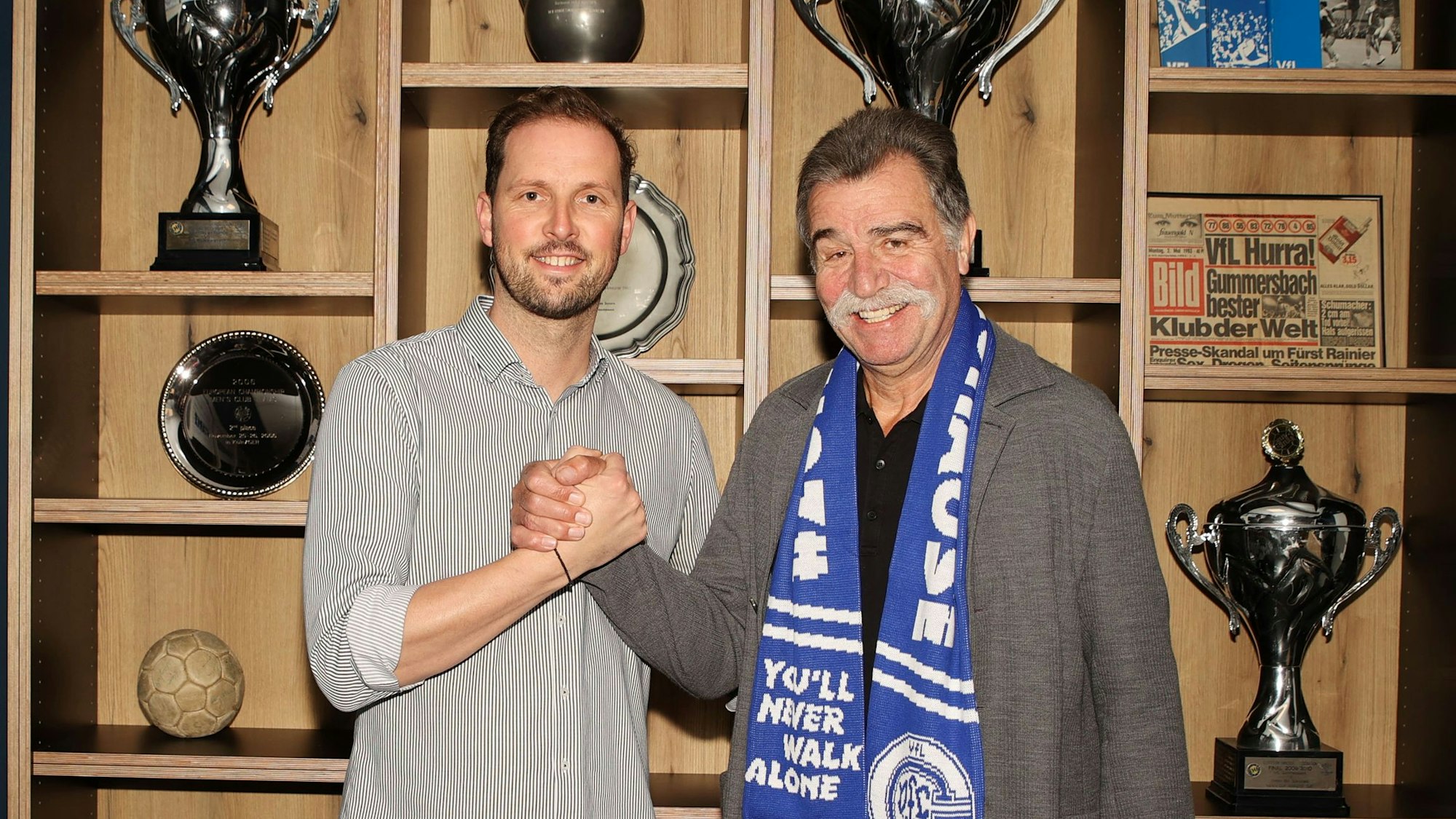 Heiner Brand und Geschäftsführer Christoph Schindler stehen vor dem Trophäenschrank des VfL Gummersbach.