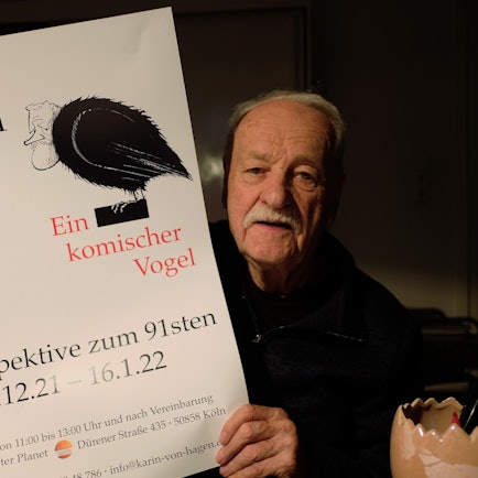 Walter Hanel hält ein Ausstellungsplakat in die Höhe.